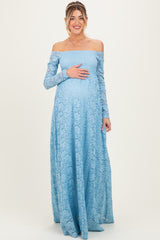 woman wearing a light blue off-the-shoulder lace maternity gown with long sleeves and cradling her baby bump