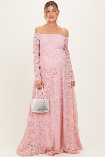 woman wearing a light pink off-the-shoulder lace maternity gown and holding a small white handbag with a visible baby bump