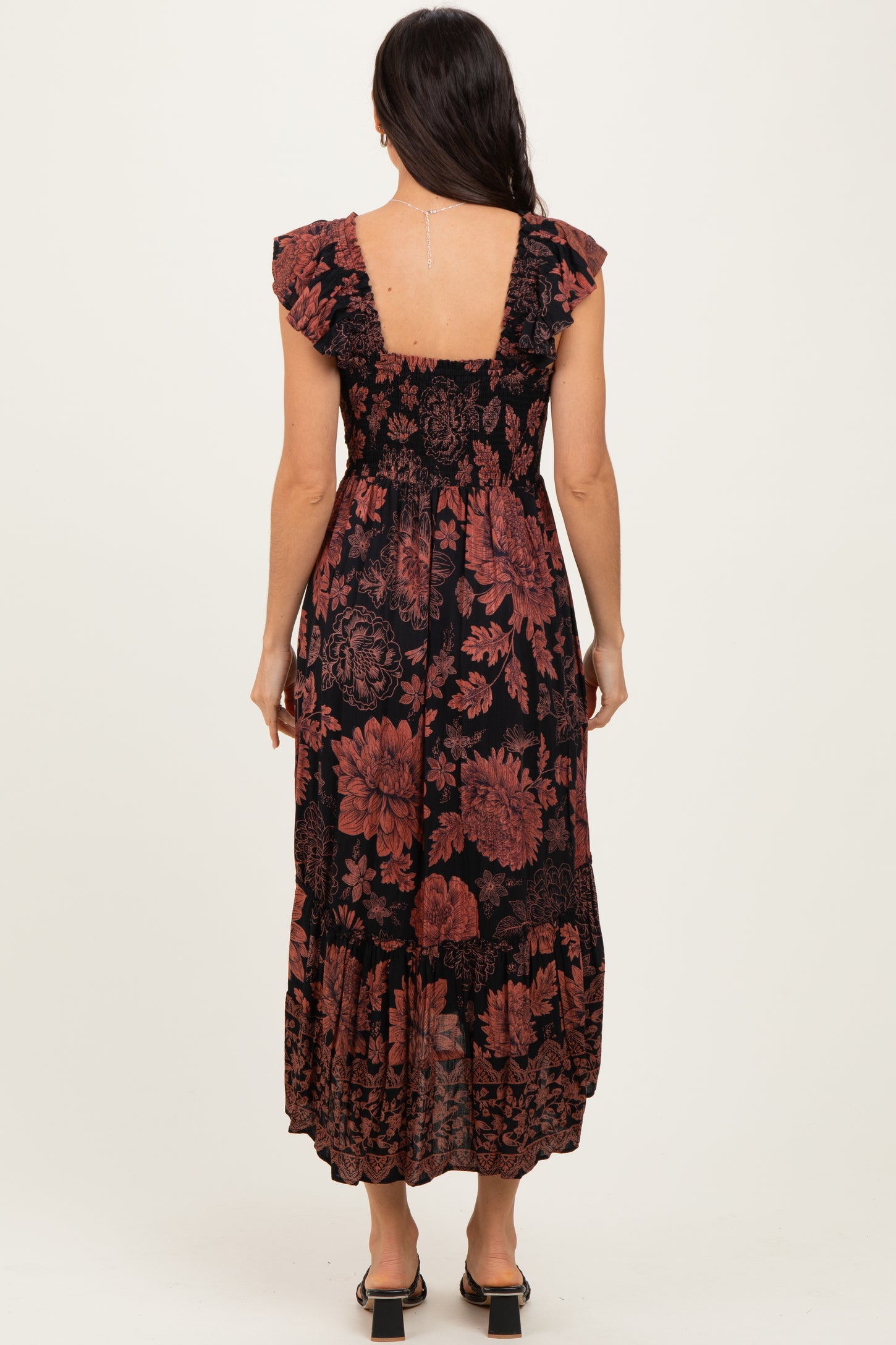 woman wearing a black floral maxi dress with ruffled sleeves and a tiered skirt, shown from the back