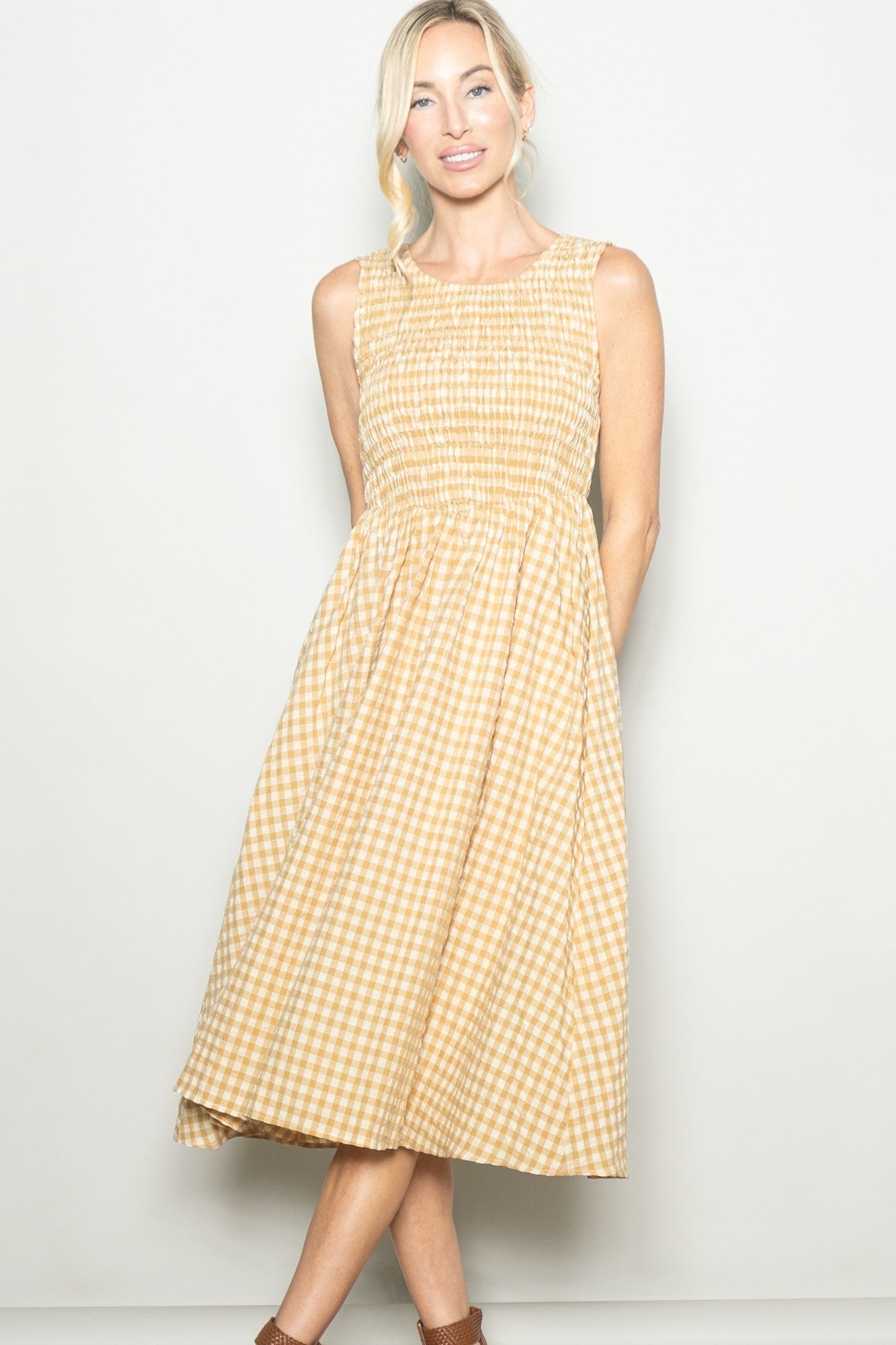 woman wearing a yellow and white gingham midi dress with a smocked bodice and sleeveless design