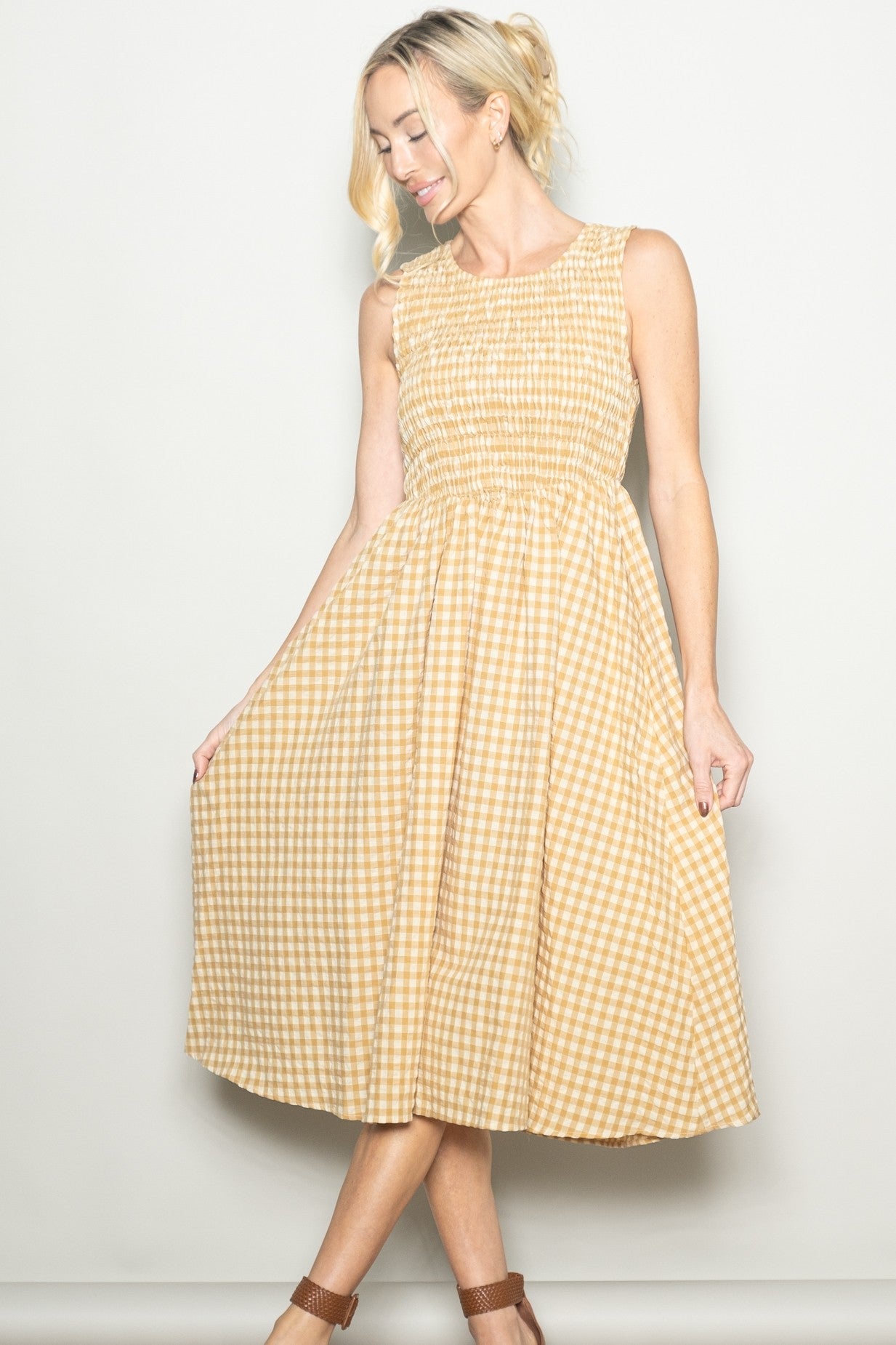 woman wearing a smocked yellow gingham dress with a flowing skirt, standing against a neutral background