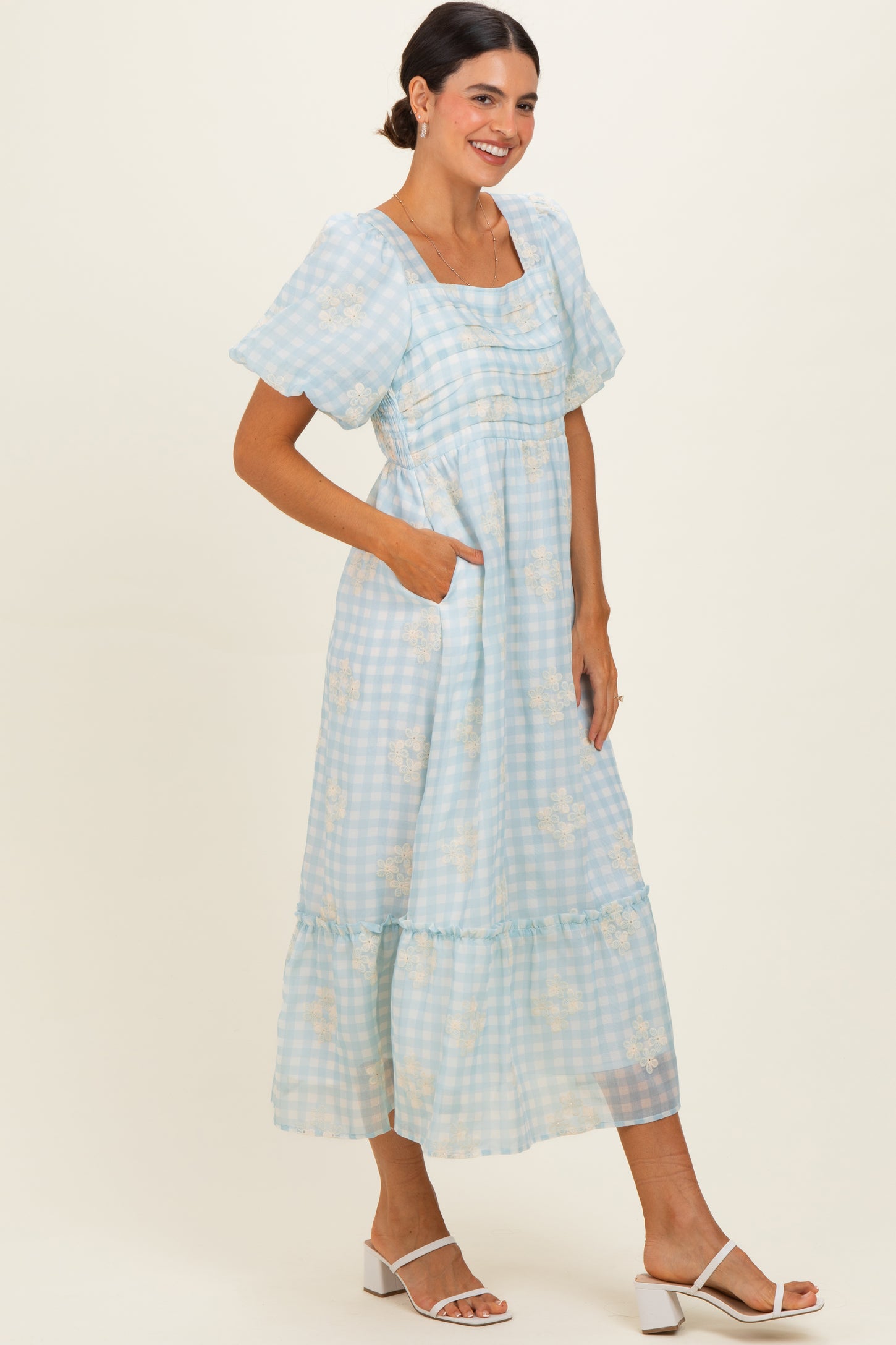 woman wearing a light blue gingham maxi dress with puff sleeves and pockets, styled with white heeled sandals