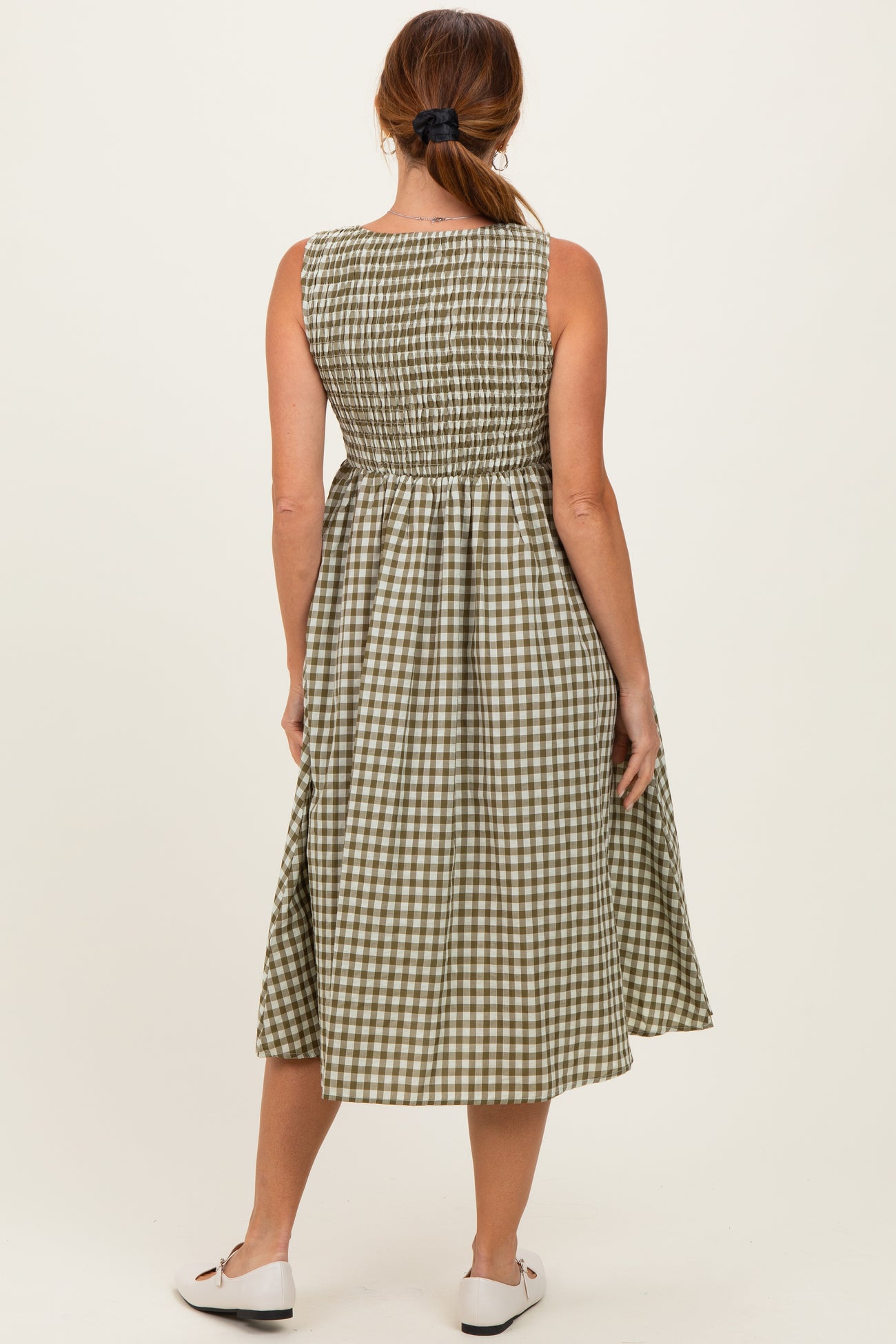 woman wearing a green and white gingham sleeveless dress with a smocked waist and flowing skirt, seen from the back