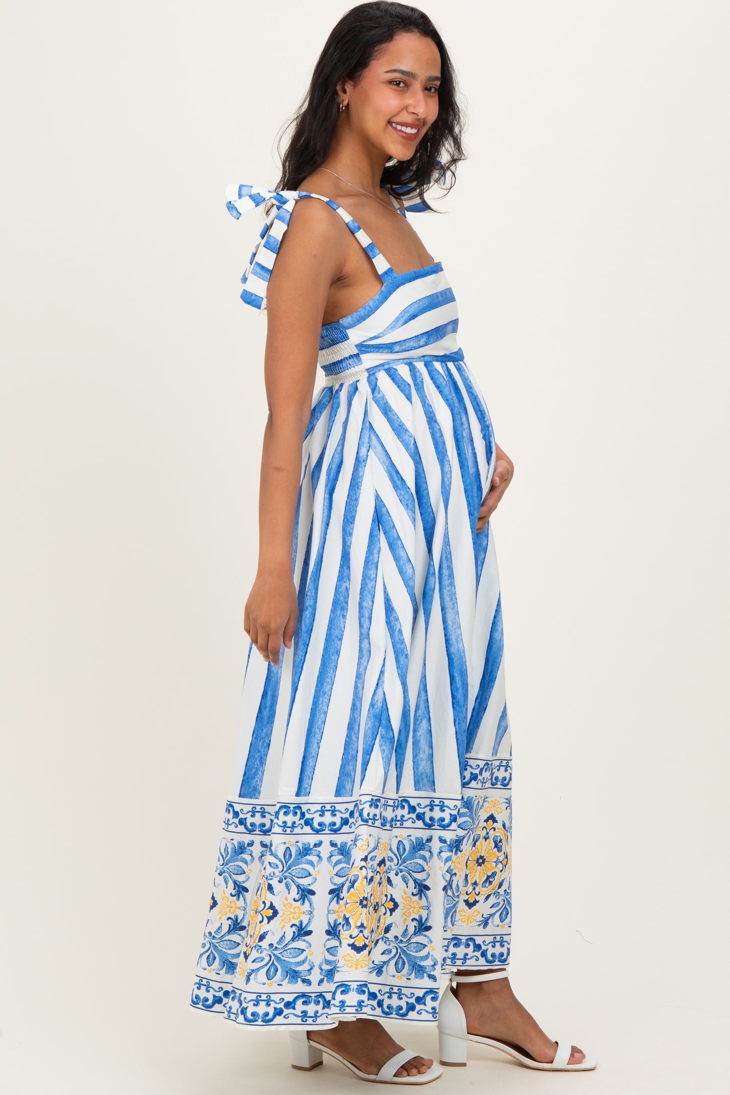 woman wearing a blue and white striped maternity maxi dress with floral details and a visible baby bump