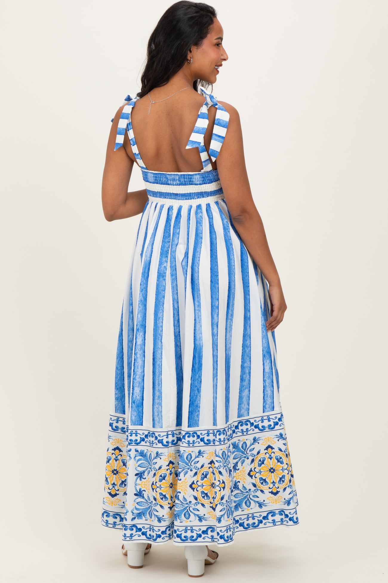 woman wearing a blue and white striped maternity maxi dress with floral accents and tie shoulder straps