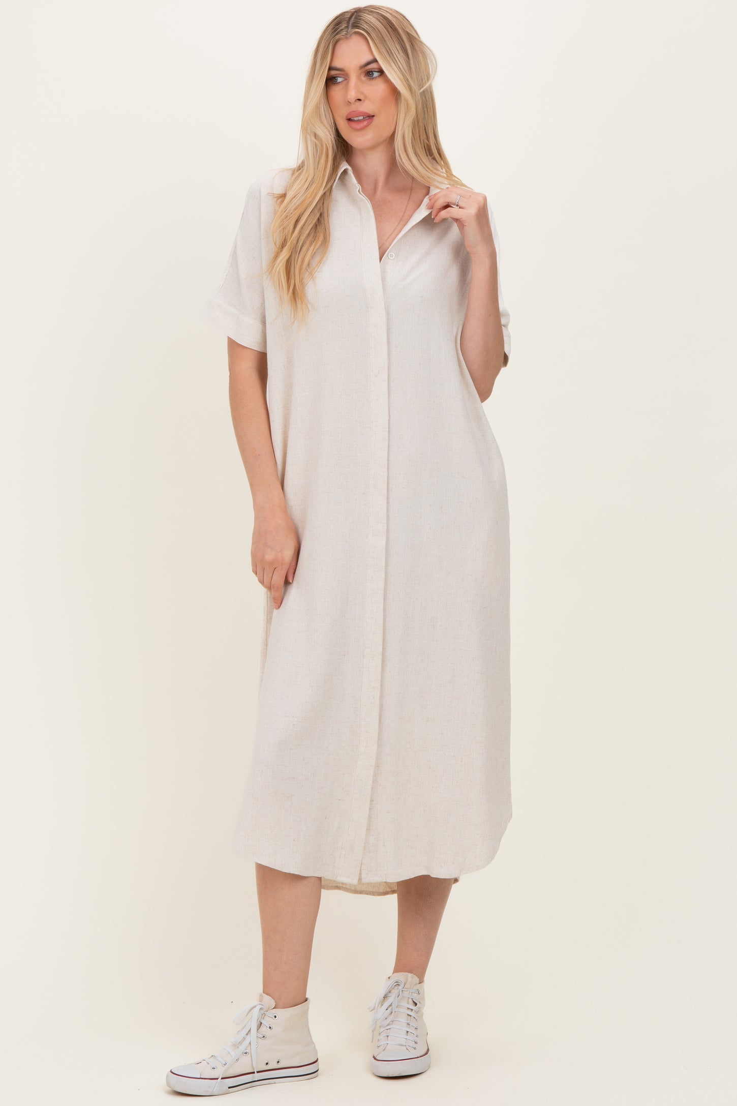 woman wearing a light beige button-up midi shirt dress with short sleeves and white sneakers
