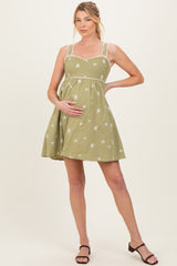 woman wearing a green maternity dress with decorative embroidery and spaghetti straps, holding her baby bump