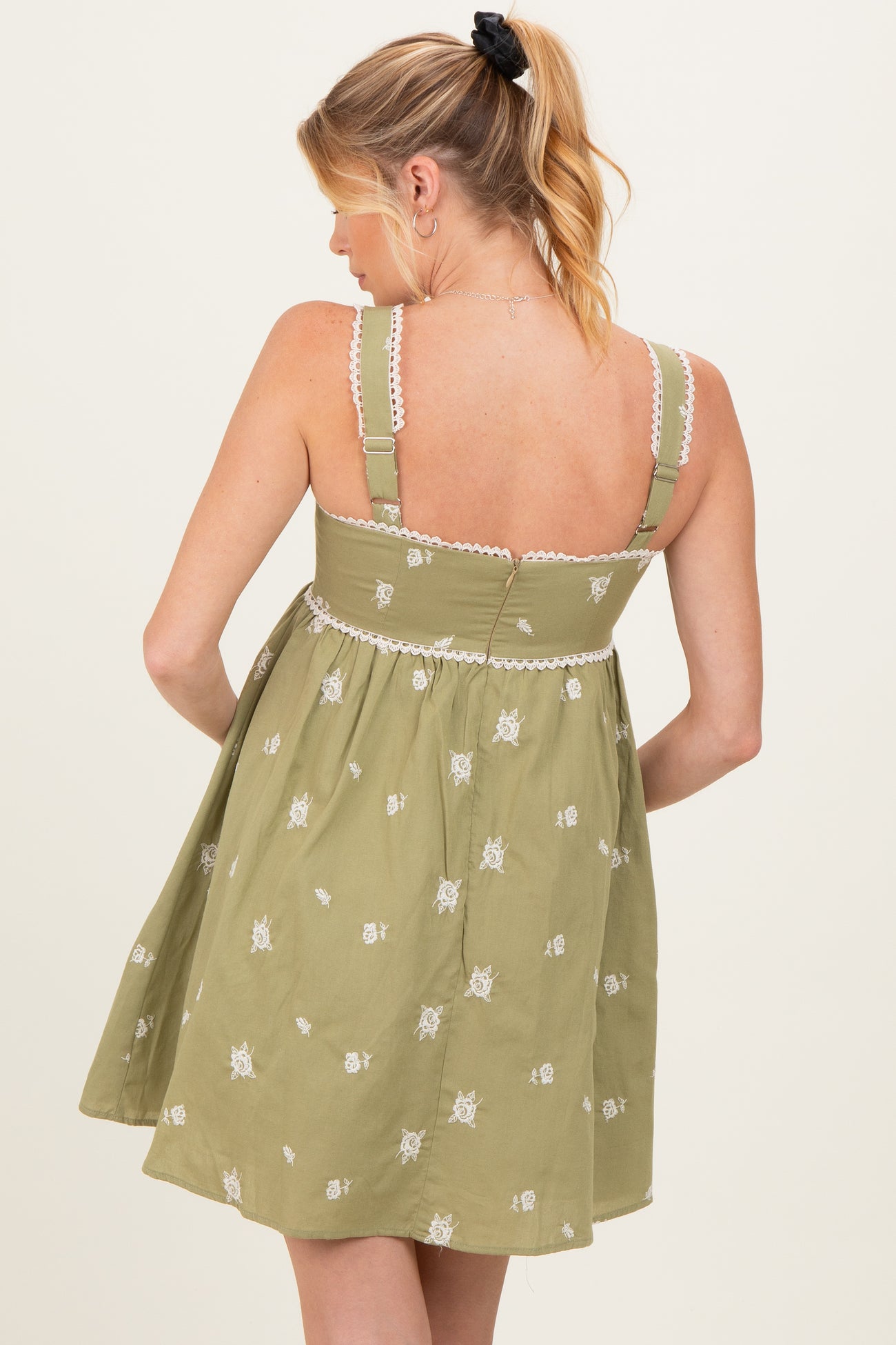 woman wearing a green embroidered maternity dress with adjustable straps and a flowy silhouette, showing her back