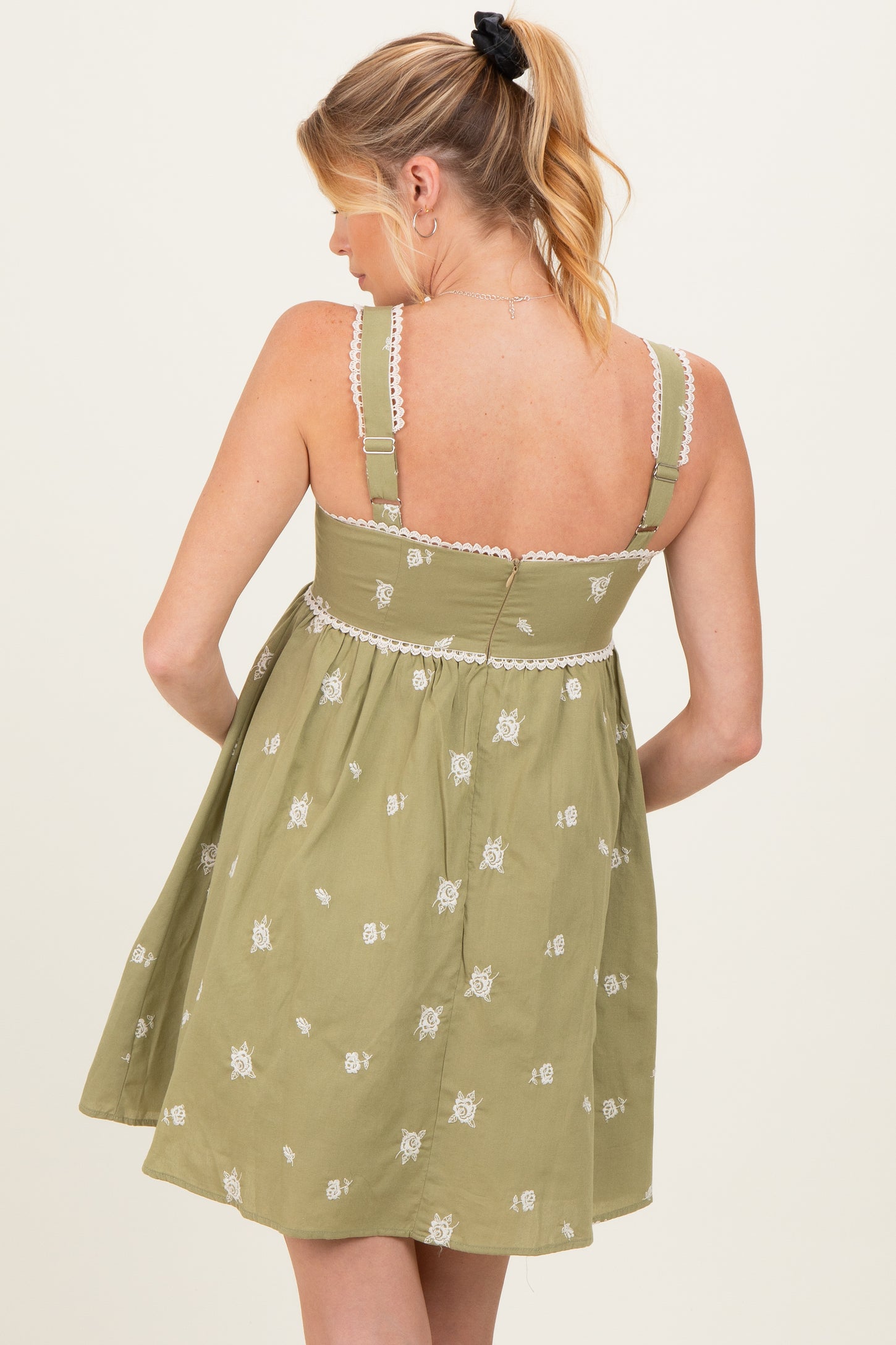 woman wearing a green embroidered maternity dress with adjustable straps and a flowy silhouette, showing her back