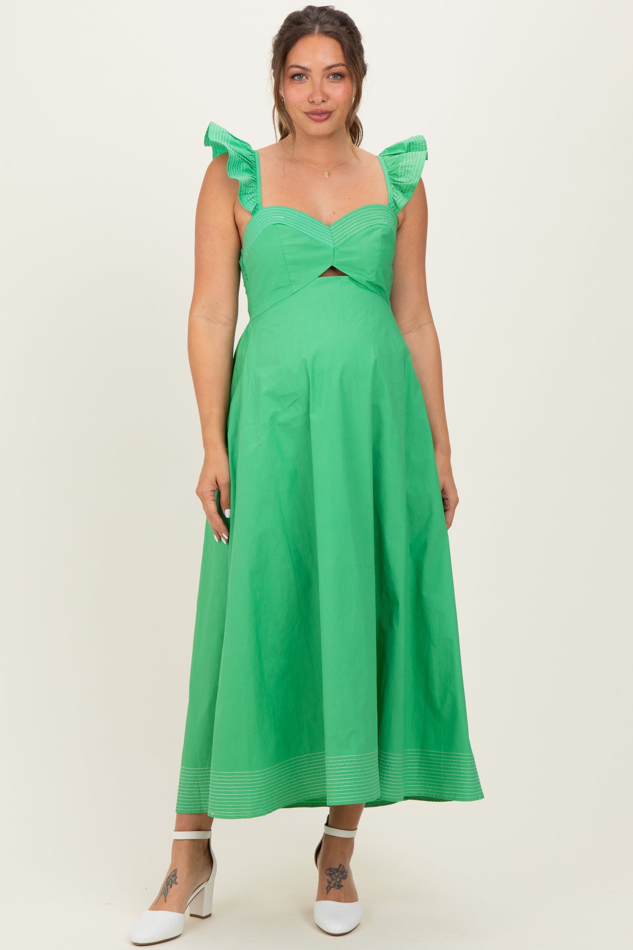 woman wearing a green maternity dress with ruffle straps and a cutout detail, standing and smiling