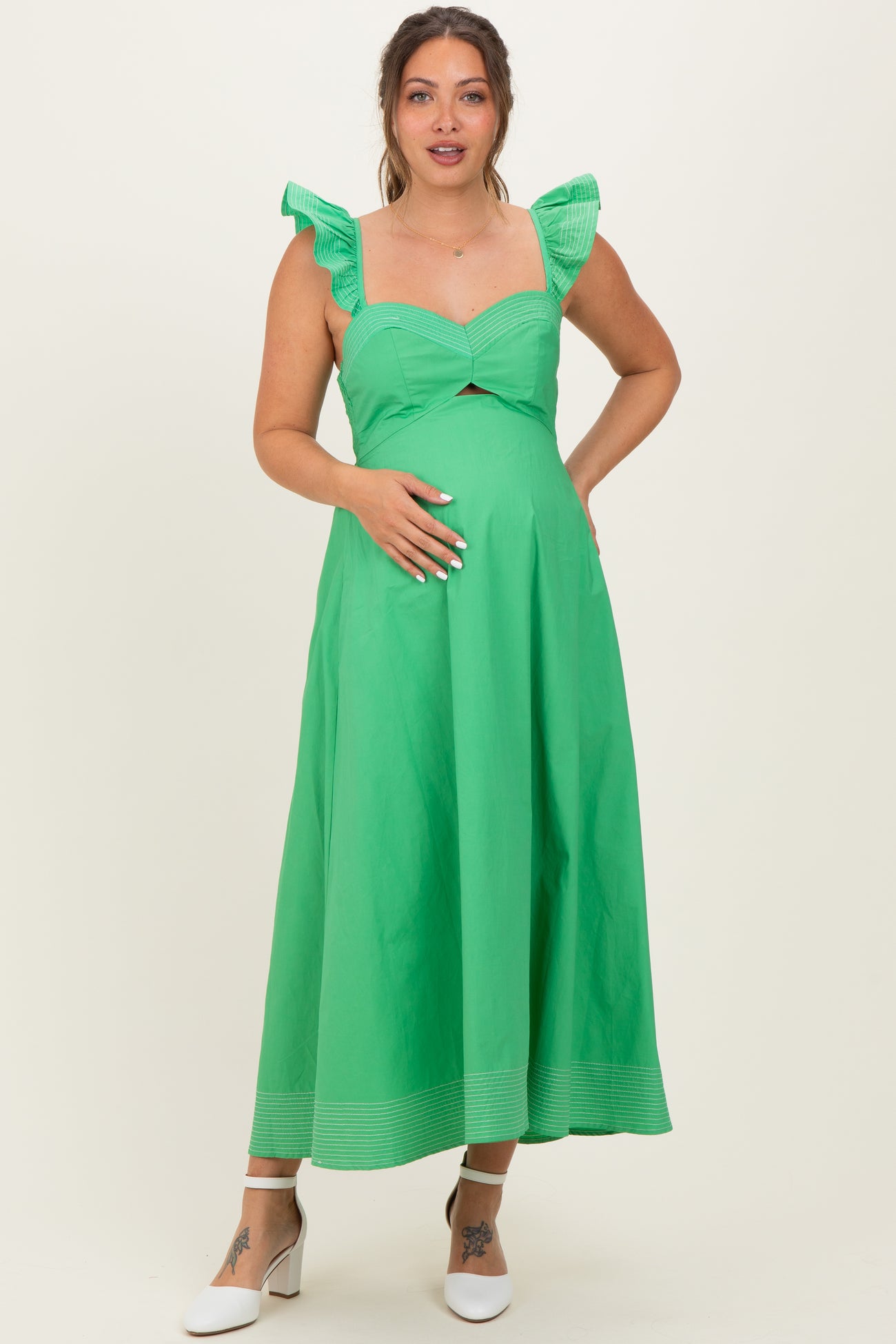woman wearing a green maternity dress with ruffle sleeves and a cutout under the bust, highlighting her baby bump