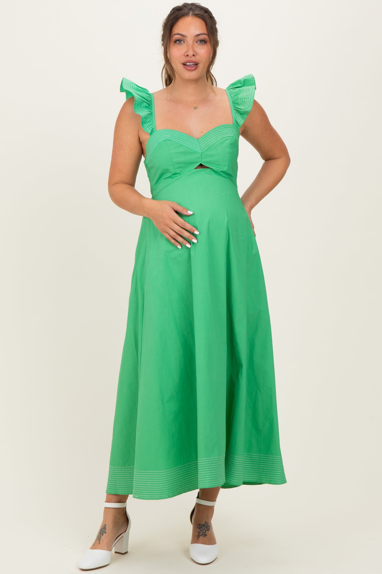 woman wearing a green maternity dress with ruffle sleeves and a cutout under the bust, highlighting her baby bump