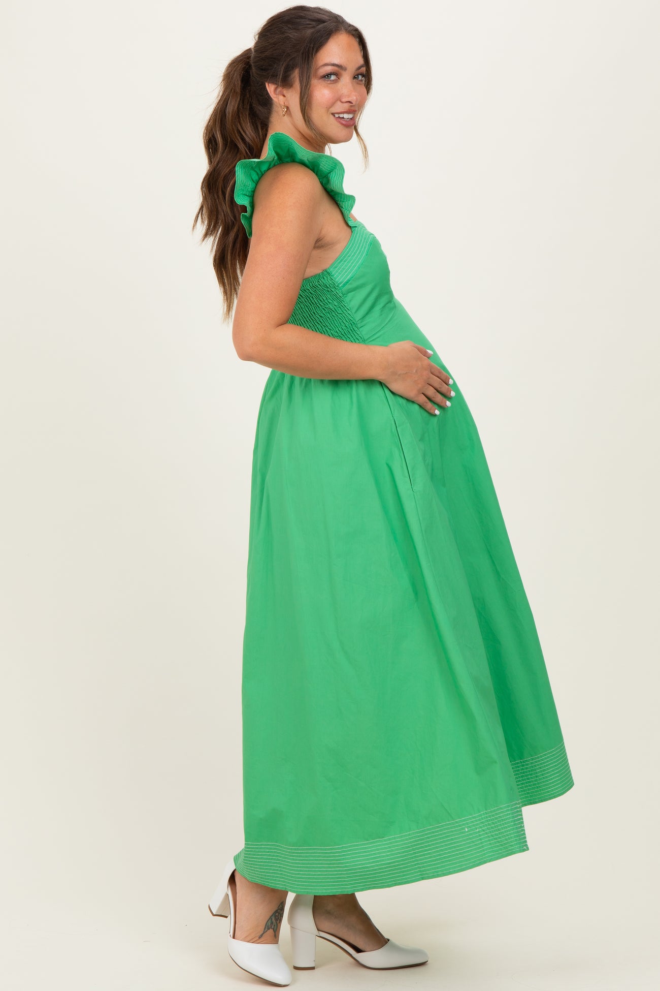 woman wearing a green maternity maxi dress with ruffle details and holding her baby bump