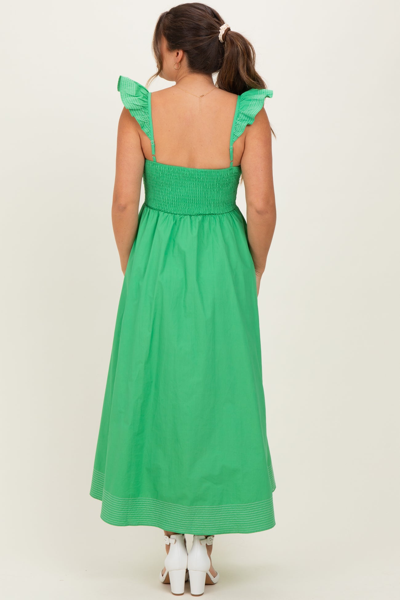 woman wearing a vibrant green maternity maxi dress with ruffle straps and smocked back, showcasing a baby bump