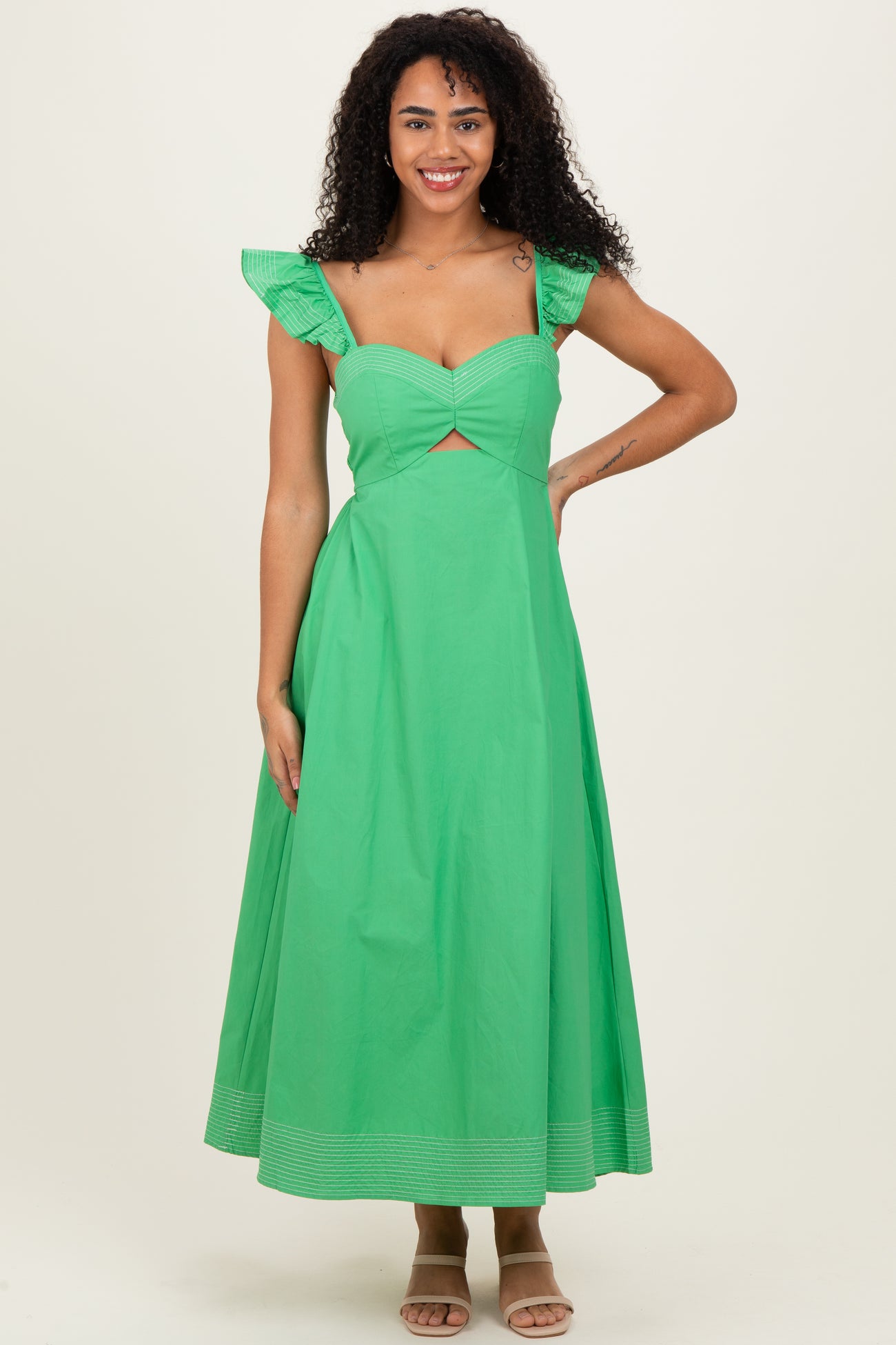woman wearing a green maxi dress with ruffle straps and a cutout detail, standing and smiling