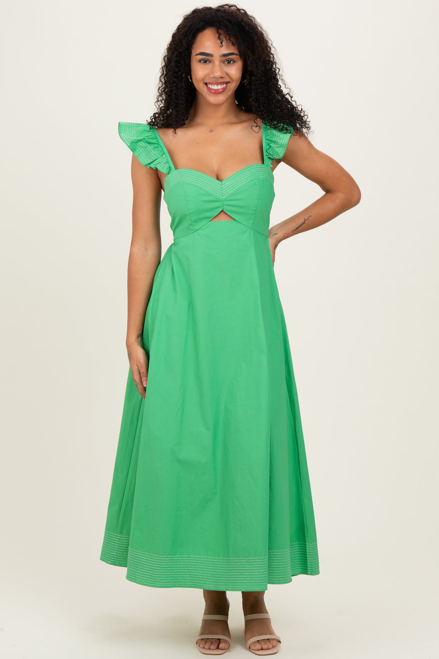 woman wearing a green maxi dress with ruffle straps and a cutout detail, standing and smiling