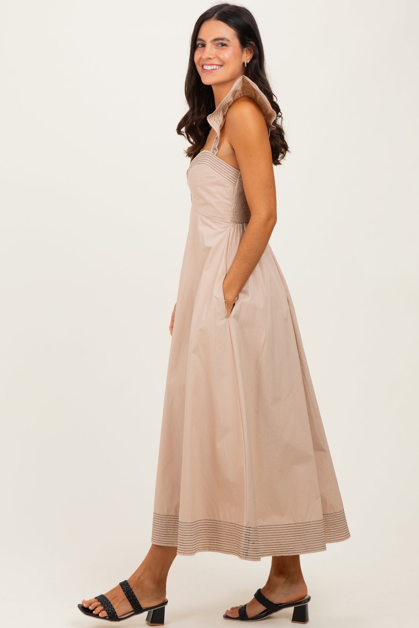 woman wearing a light beige maxi dress with a structured collar and side pockets, standing sideways