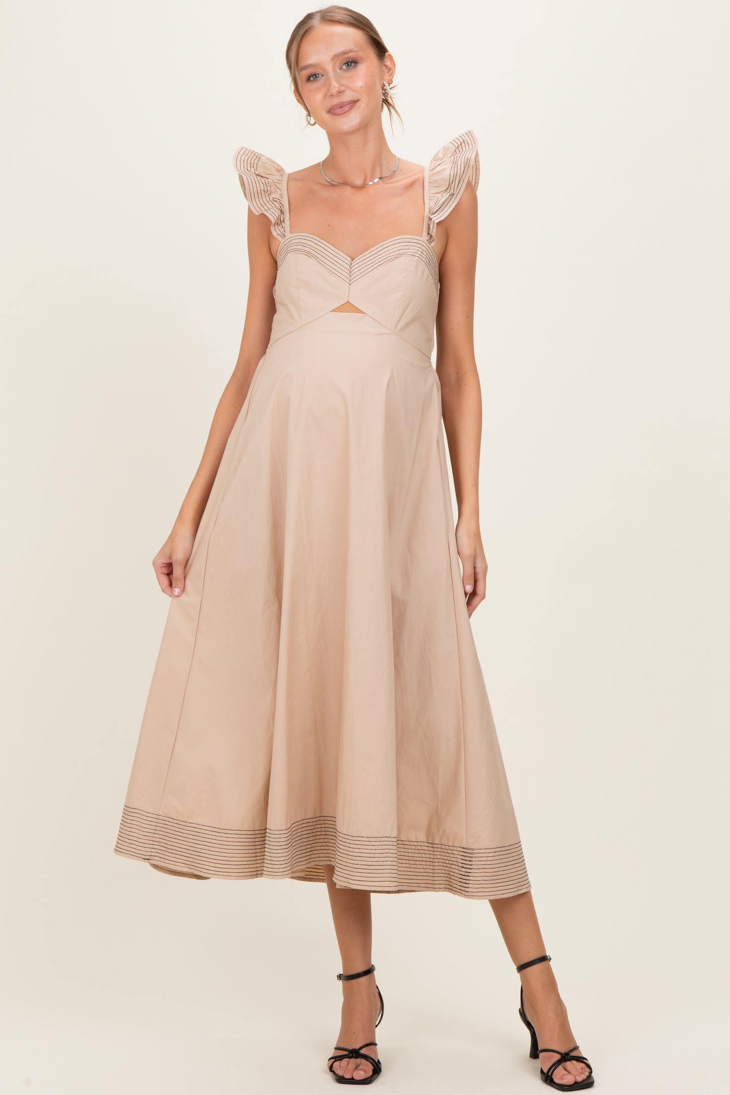 woman wearing a beige maternity dress with ruffled straps and a cutout detail, showing her baby bump