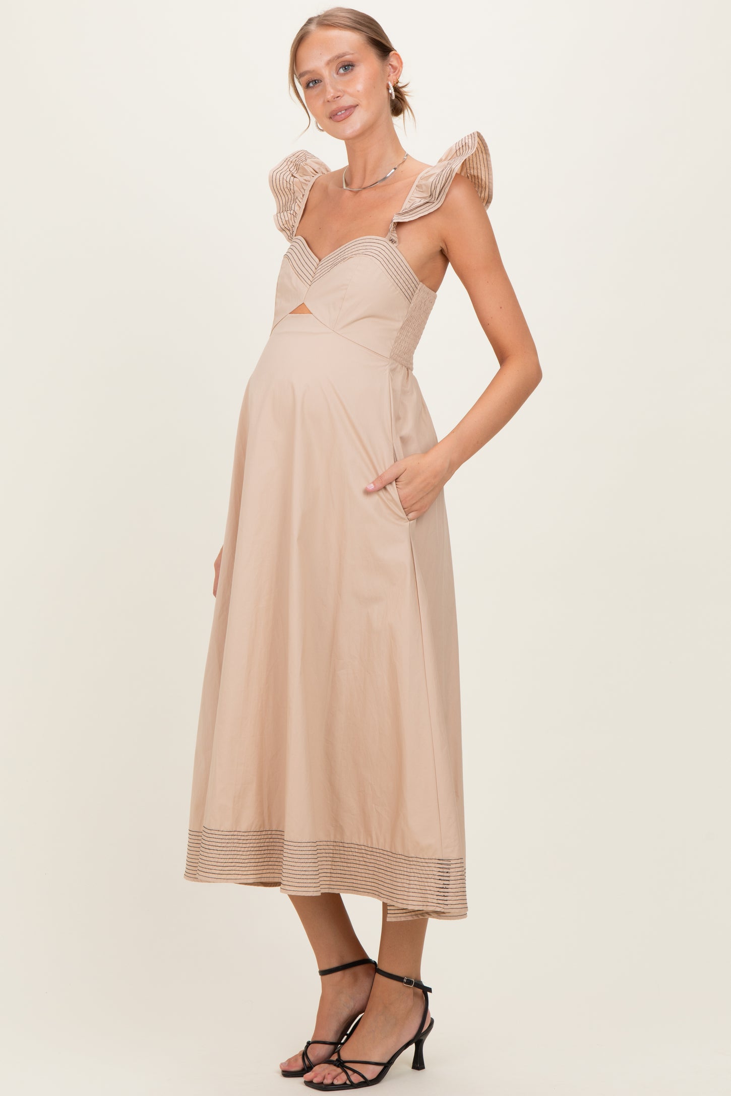 woman wearing a nude maternity dress with ruffle straps and a fitted bodice, featuring a cutout and pockets, showing baby bump
