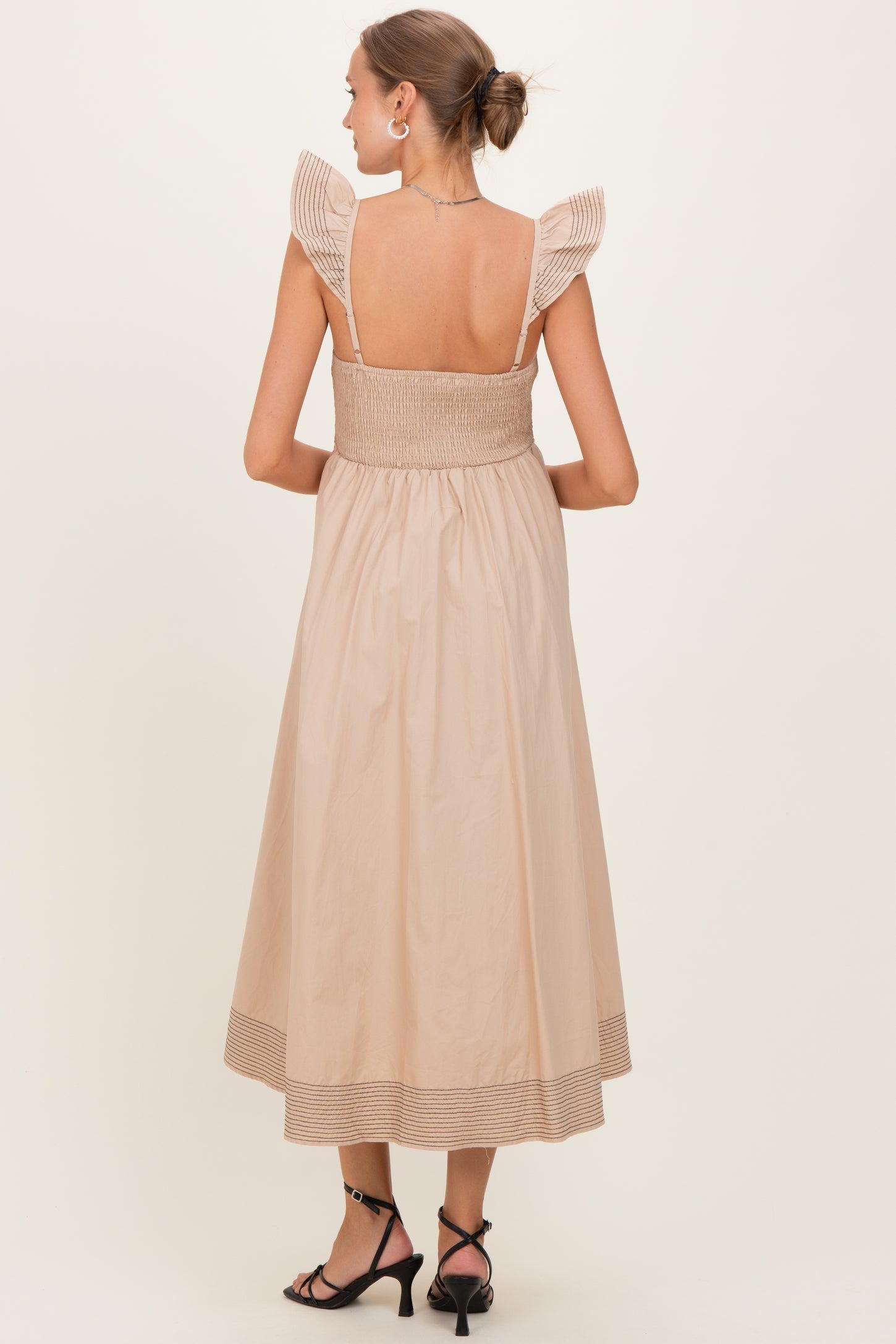 woman wearing a beige maternity dress with ruffle shoulder straps and a smocked bodice, showing a flowing skirt