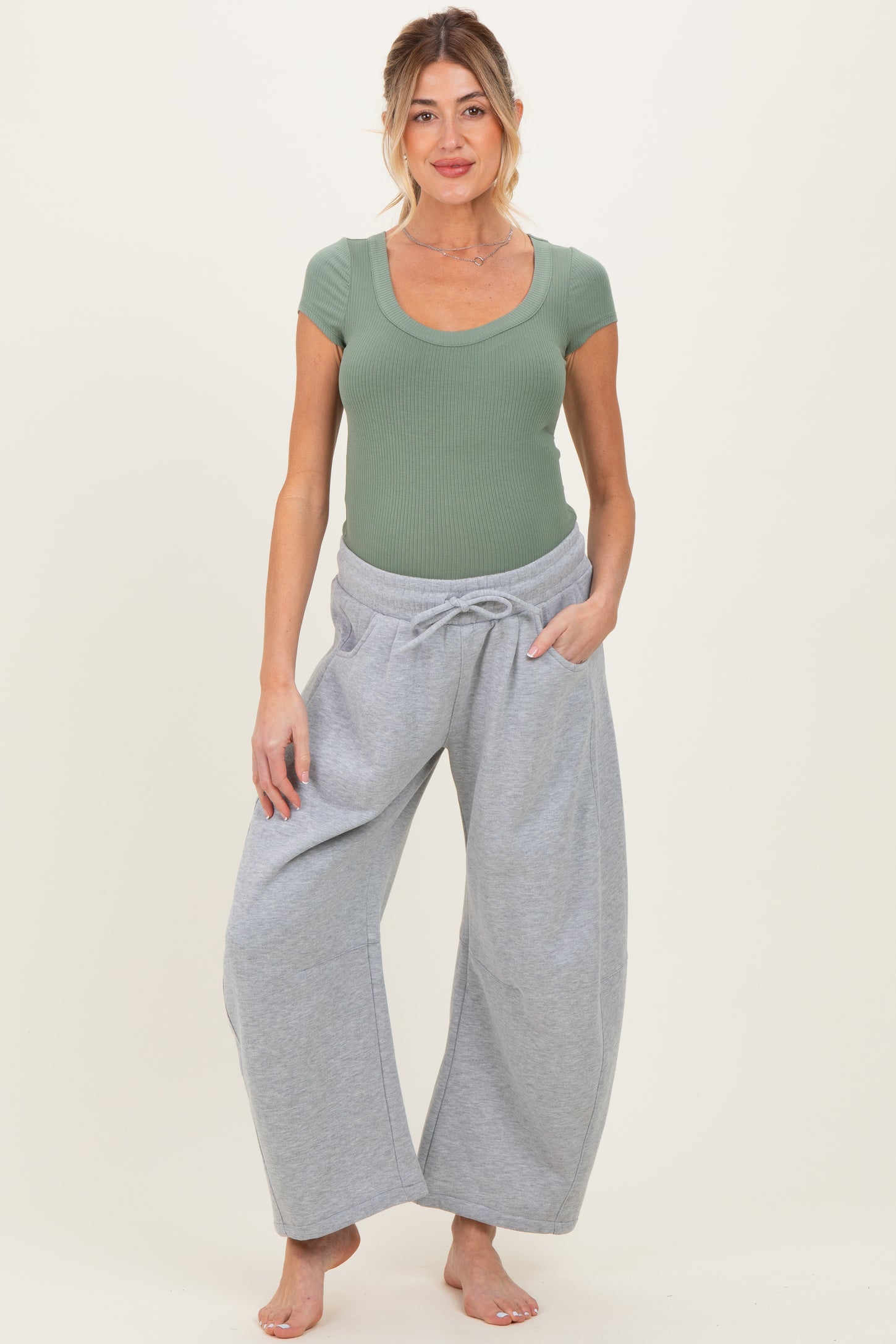 woman wearing a green ribbed short sleeve maternity top and gray wide-leg pants, showcasing a visible baby bump