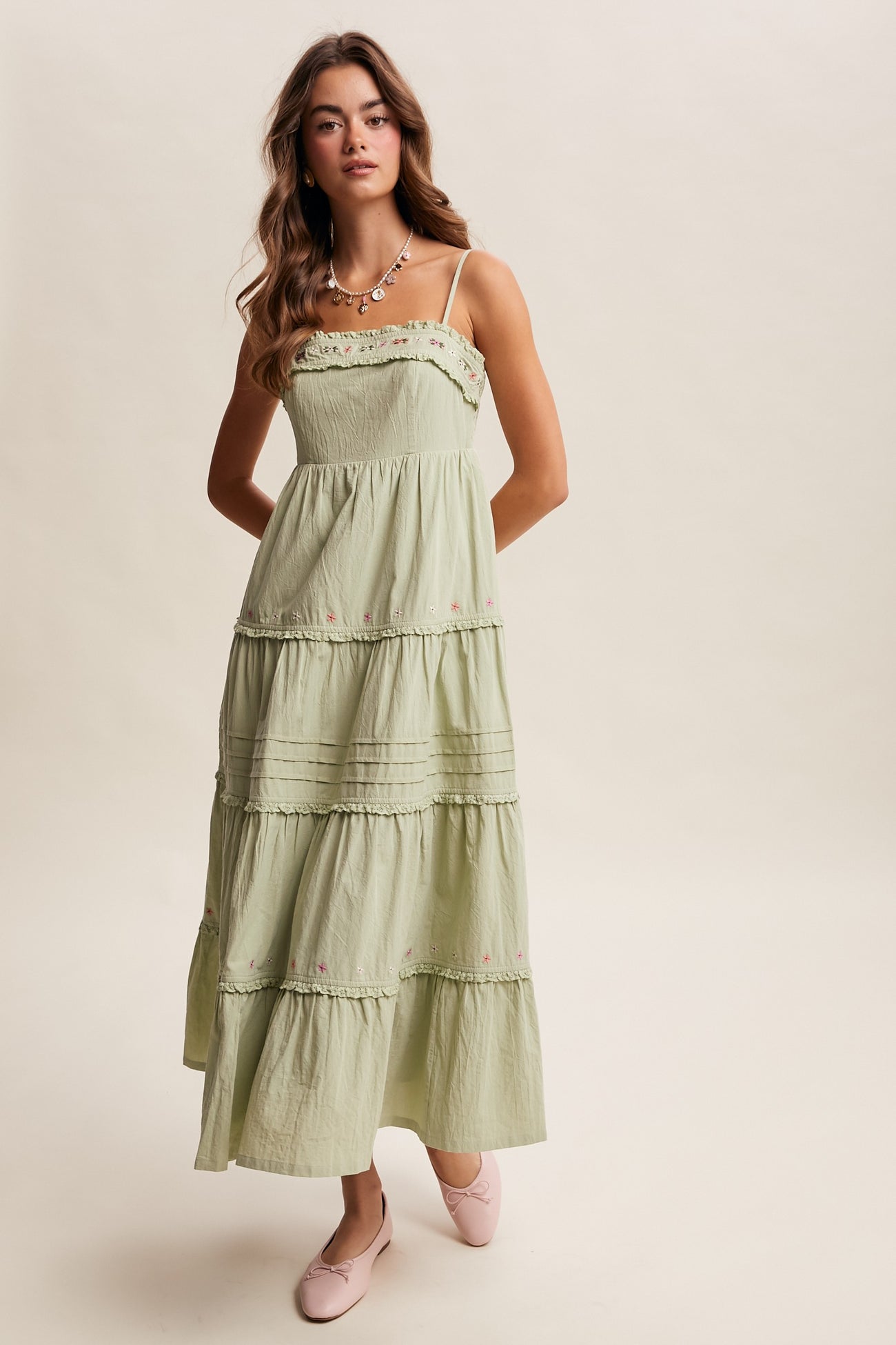 woman wearing a light green tiered maxi dress with floral embroidery and thin straps, paired with pink flats