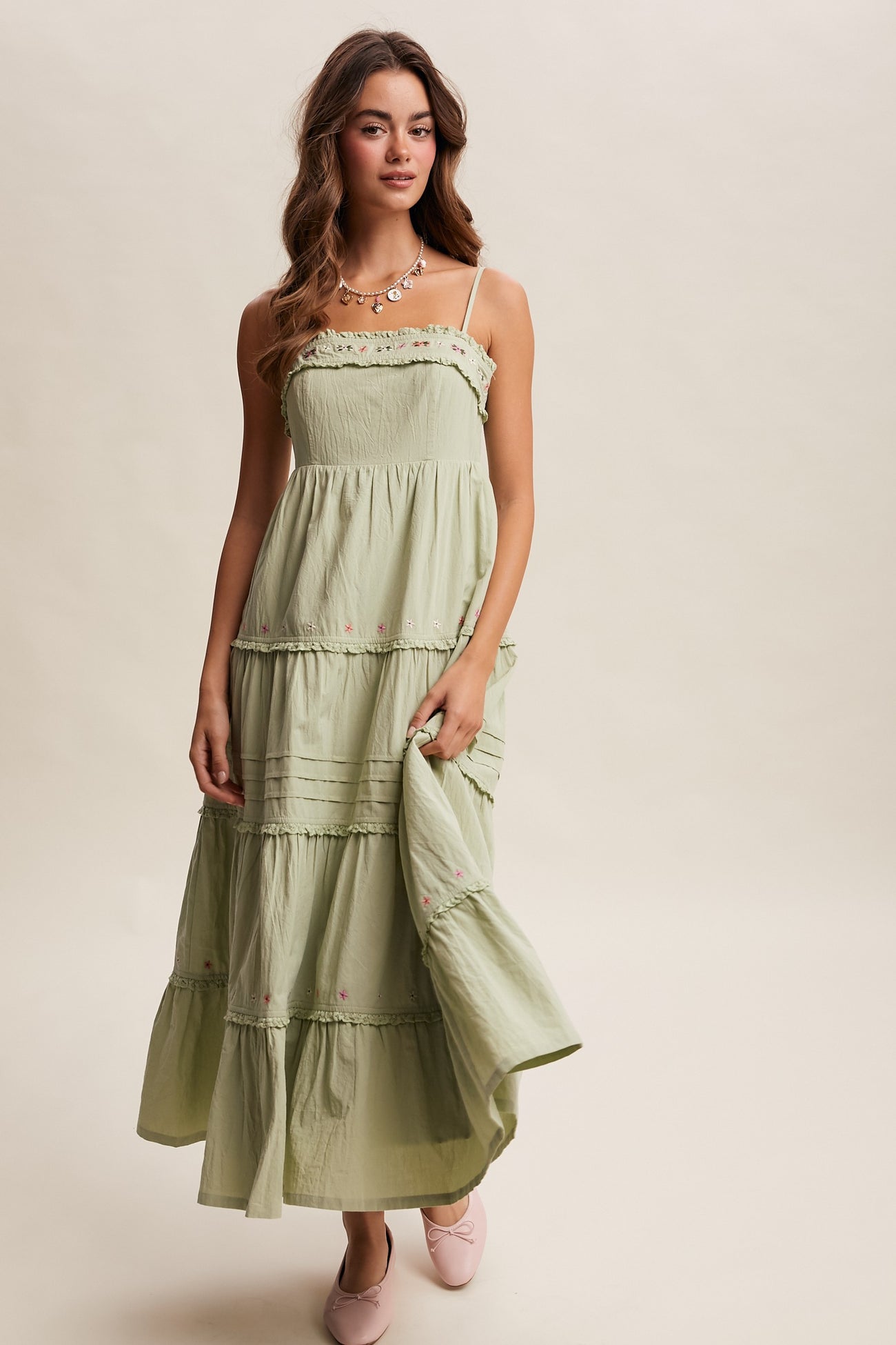 woman wearing a light green maxi dress with straps, ruffled tiers, and floral embroidery, styled with pink flats