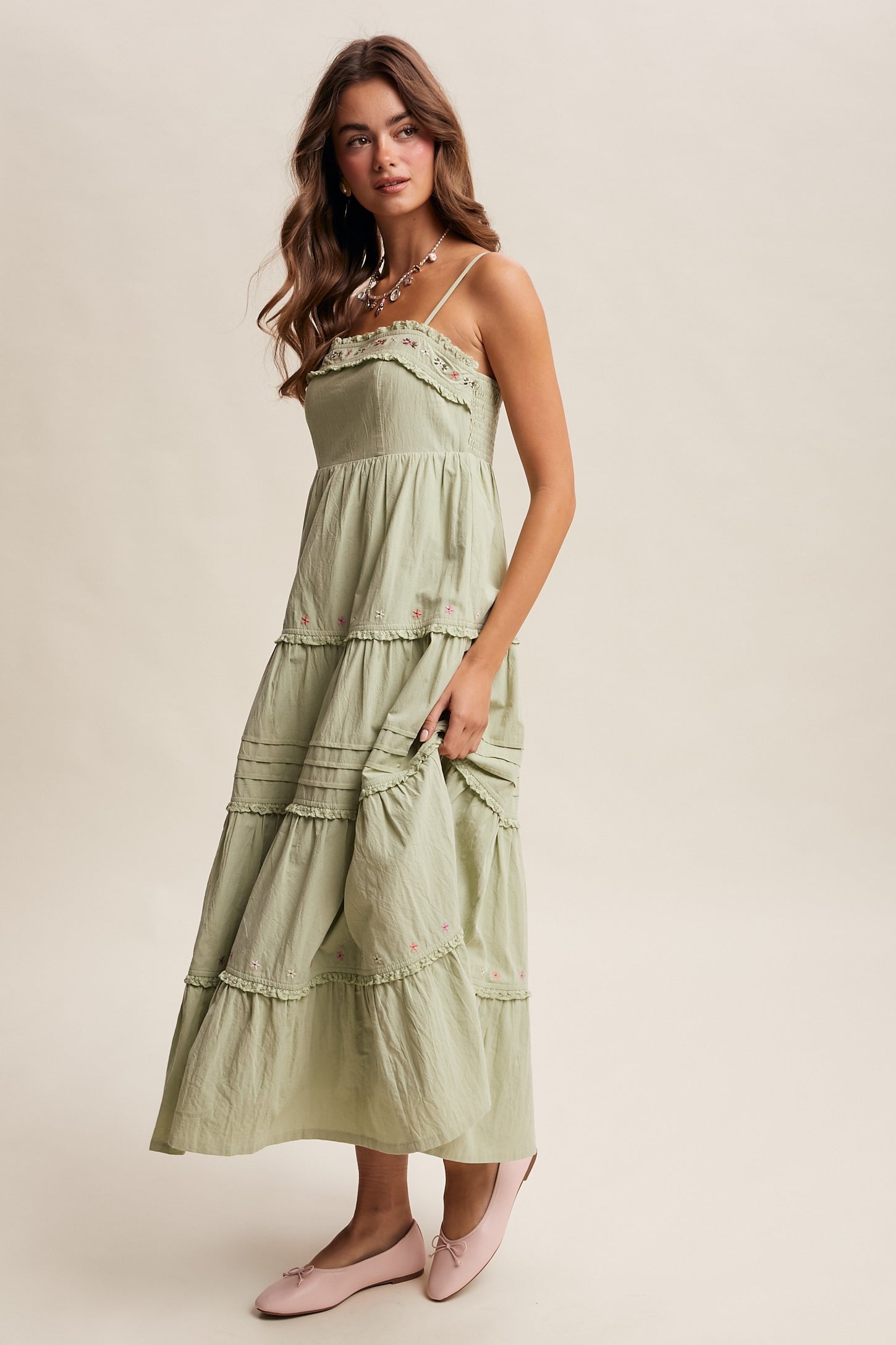 woman wearing a light green spaghetti strap maxi dress with tiered layers and floral embroidery, styled with pink flats