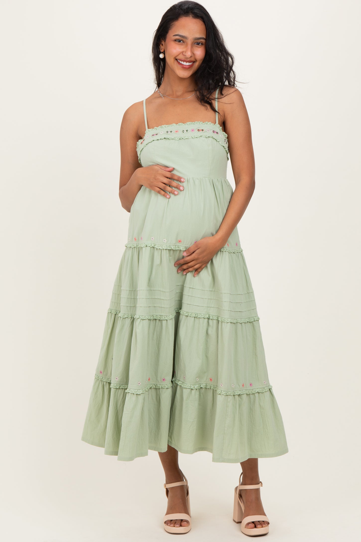 woman wearing a light green tiered maternity dress with floral details and a baby bump visible
