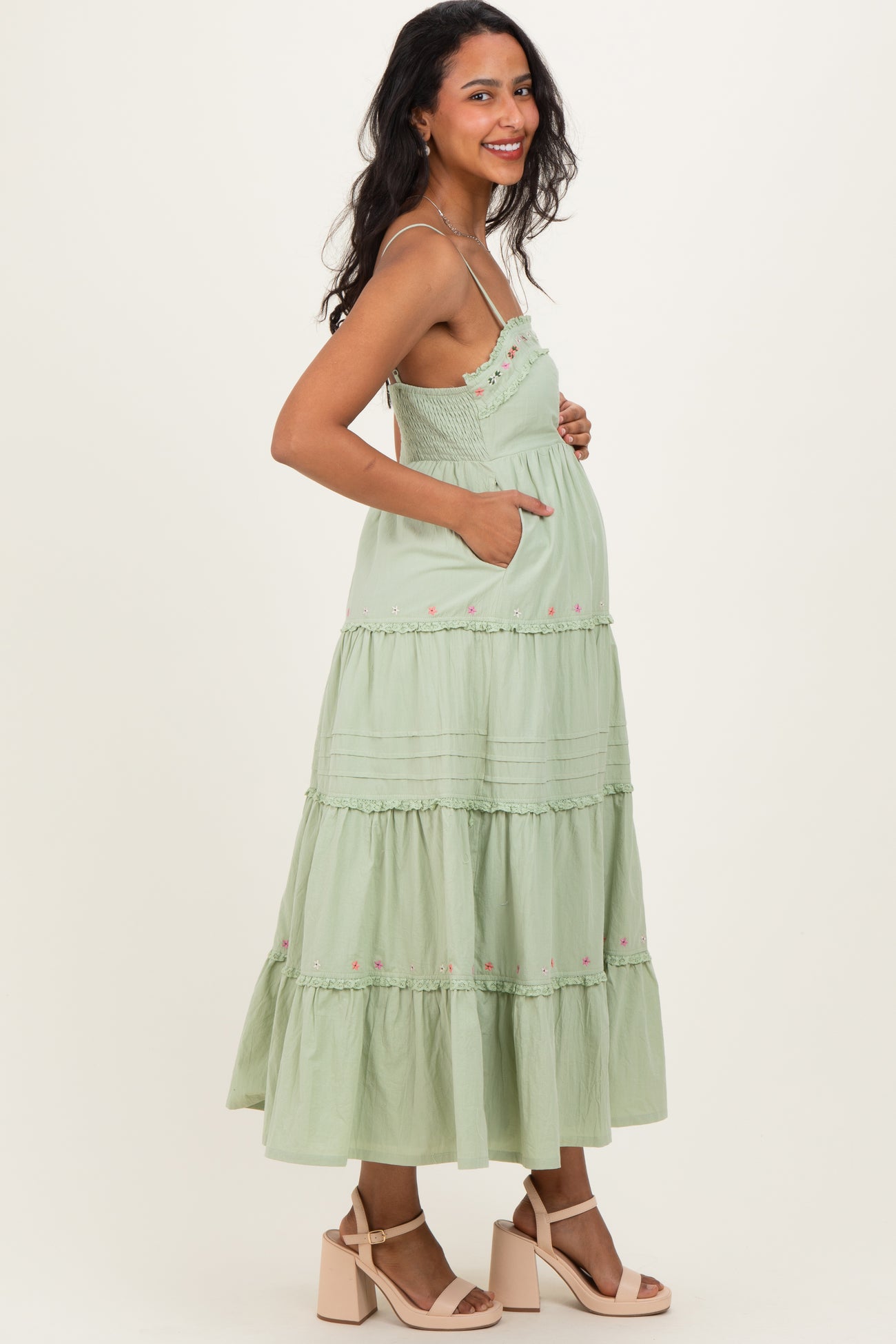 woman wearing a light green tiered maternity dress with pockets and floral embroidery, showing a baby bump