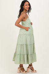 woman wearing a light green tiered maternity dress with pockets and floral embroidery, showing a baby bump