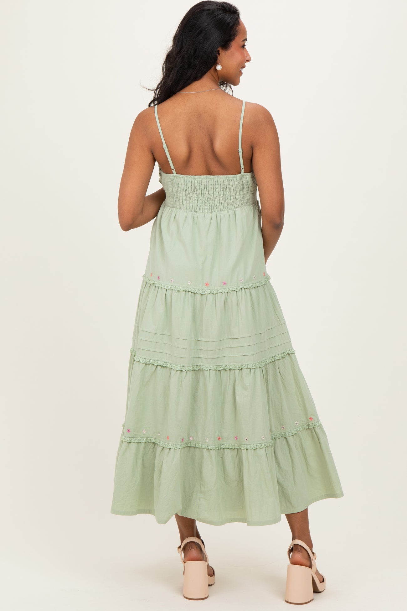 woman wearing a light green tiered maternity dress with smocked back and adjustable straps, showcasing floral embroidery