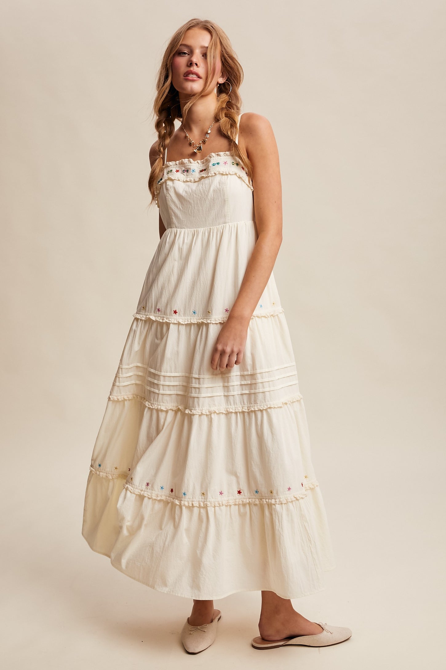 woman wearing a white tiered maxi dress with colorful embroidery and slipping off the shoulder straps