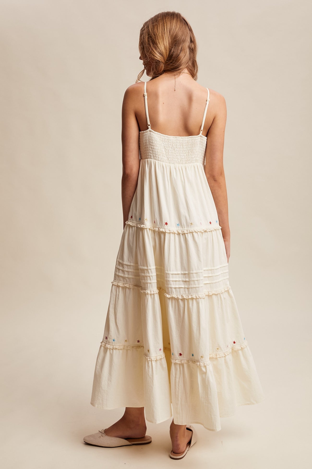 woman wearing a cream-colored tiered maxi dress with a smocked bodice and colorful floral embroidery at the hem.