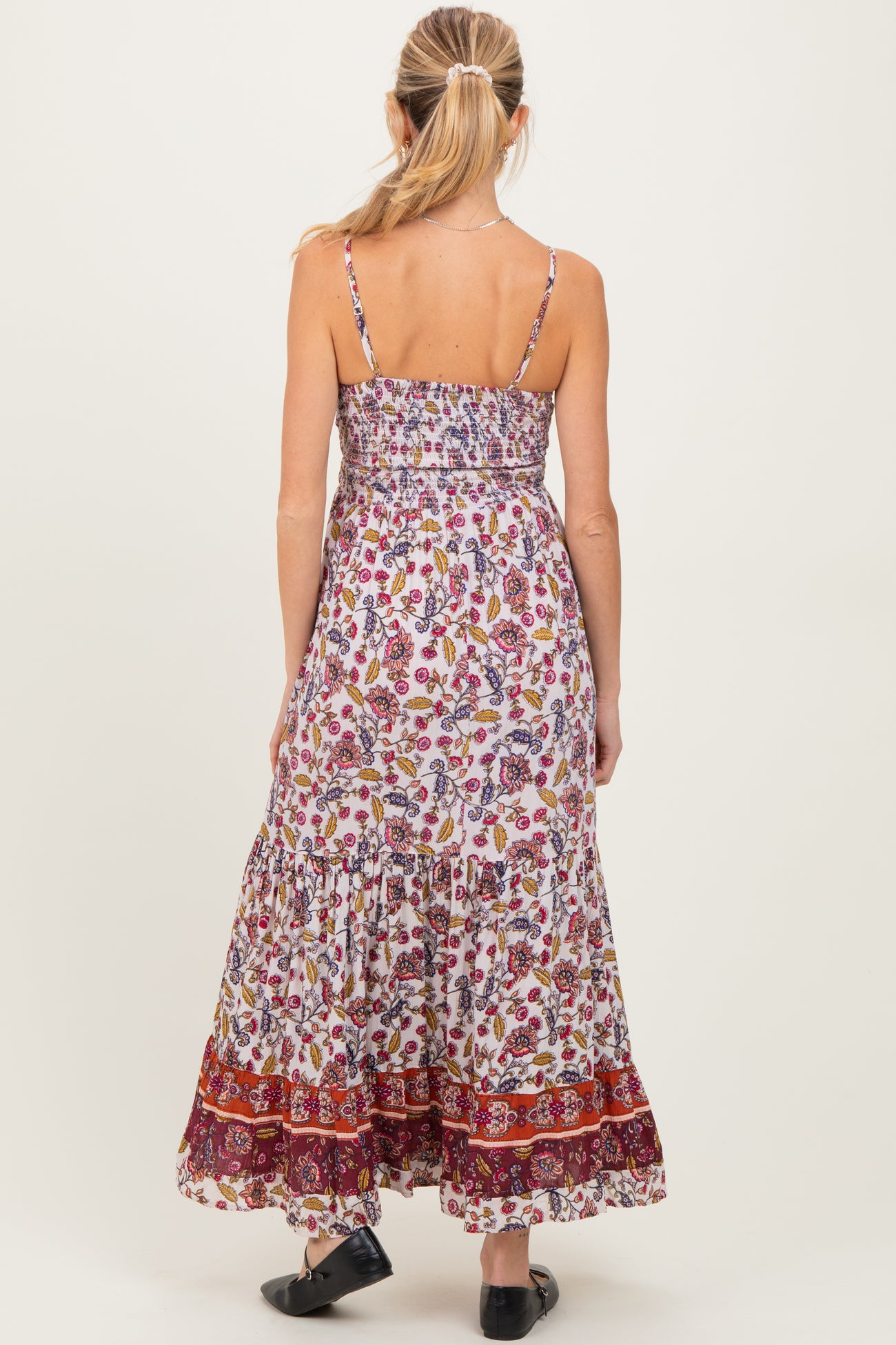woman wearing a floral maxi maternity dress with adjustable straps and a tiered hem, showing a baby bump from the back