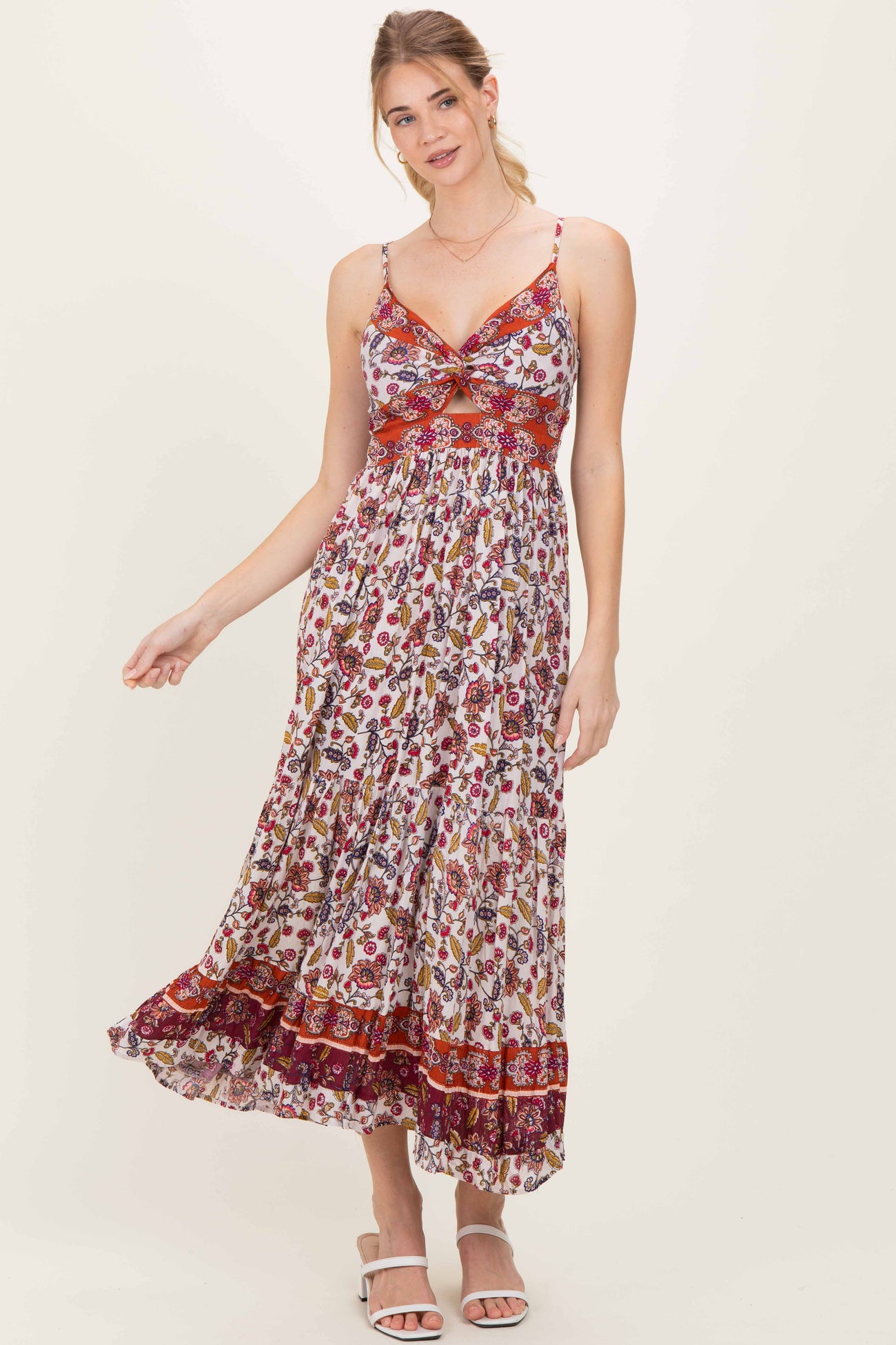 woman wearing a floral print maxi dress with a cinched bodice and spaghetti straps, standing and smiling