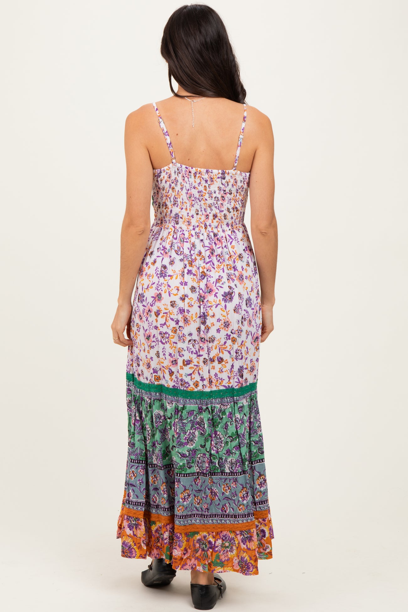 woman wearing a floral maxi dress with thin straps and a layered patterned skirt, view from the back