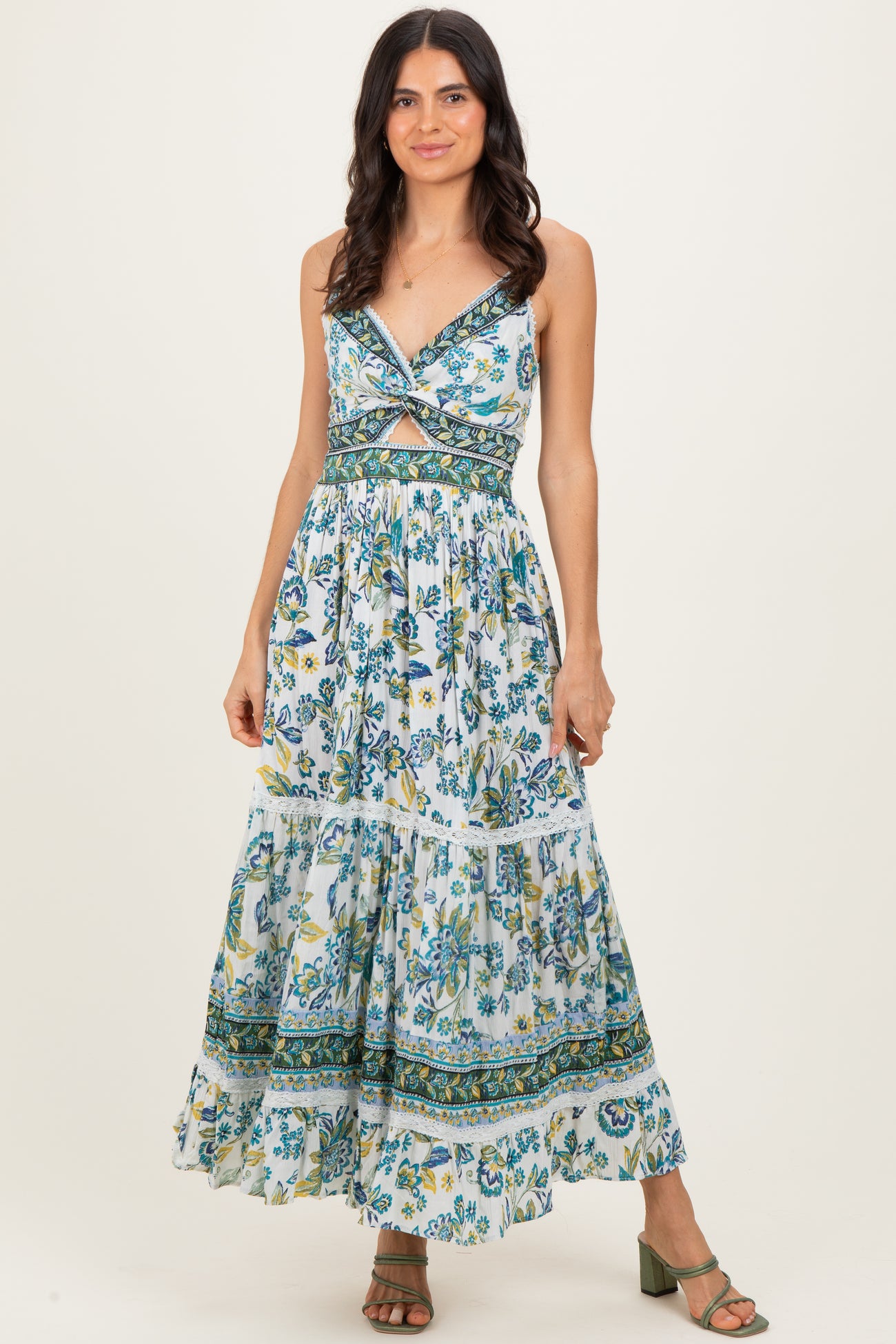 woman wearing a floral maxi dress with a front twist and tiered skirt, styled with green heeled sandals