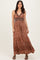 woman wearing a bohemian style brown maxi dress with a v-neck and intricate patterns, standing and smiling