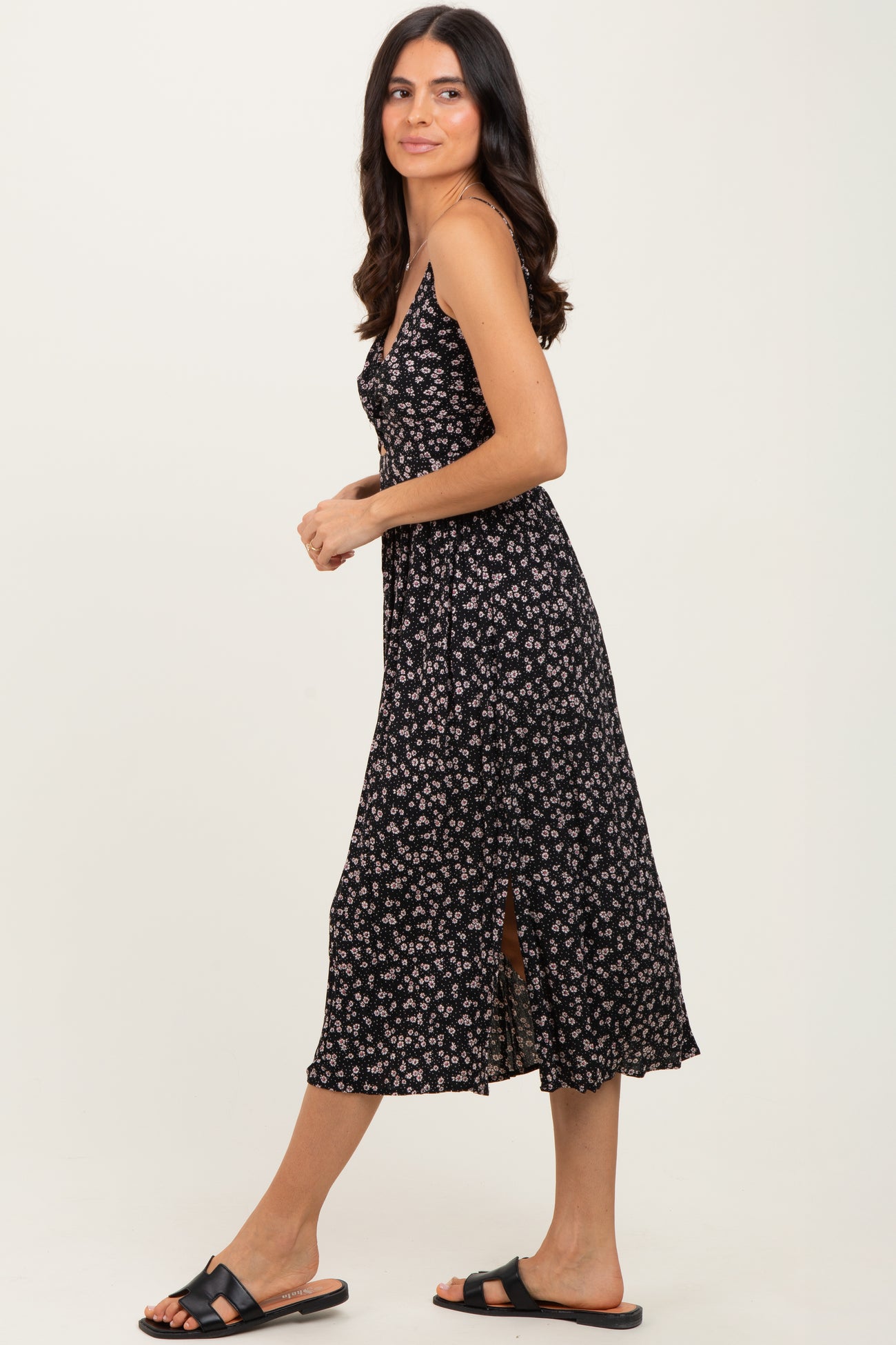 woman wearing a black floral midi dress with spaghetti straps and a side slit, paired with black slide sandals