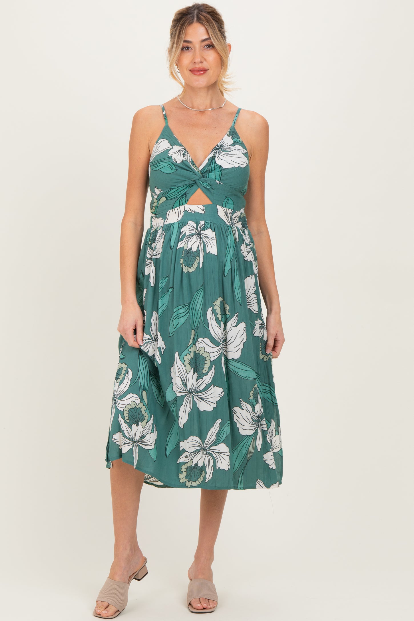 woman wearing a green floral print maternity dress with a twisted front and sleeveless design