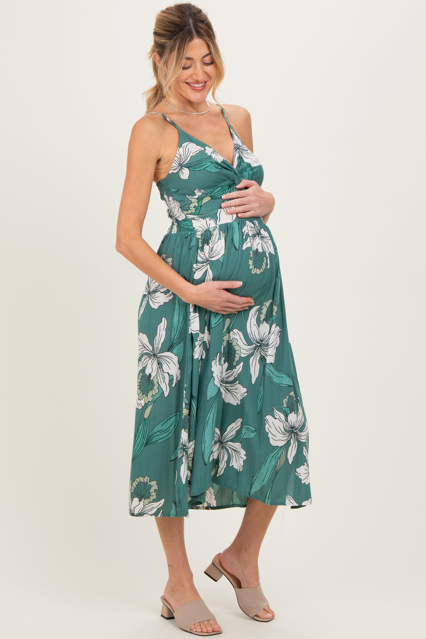 woman wearing a green floral maternity dress with a V-neckline and holding her baby bump