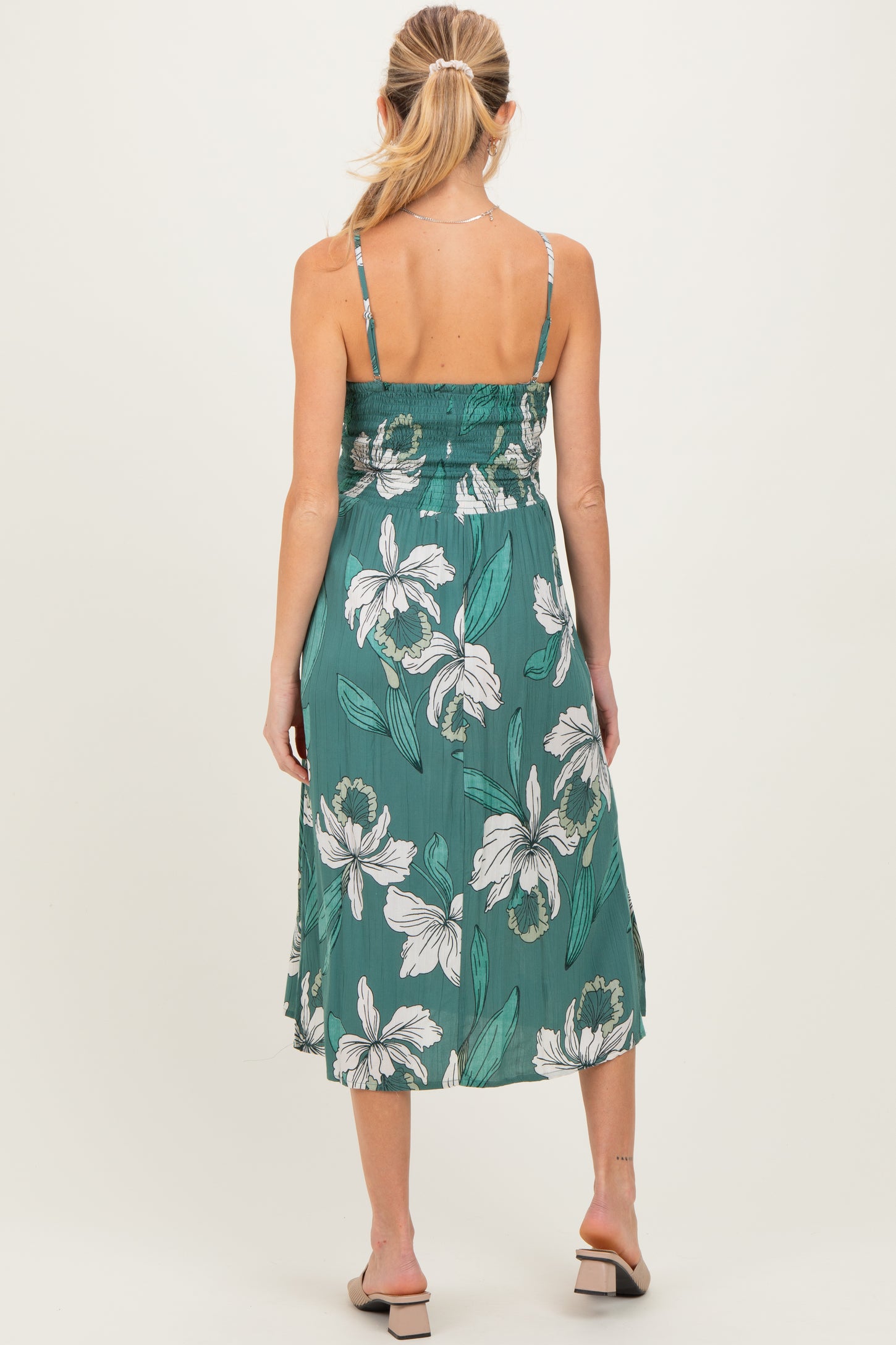 woman wearing a green floral maternity dress with a smocked bodice and flowy skirt, showing off her baby bump from the back
