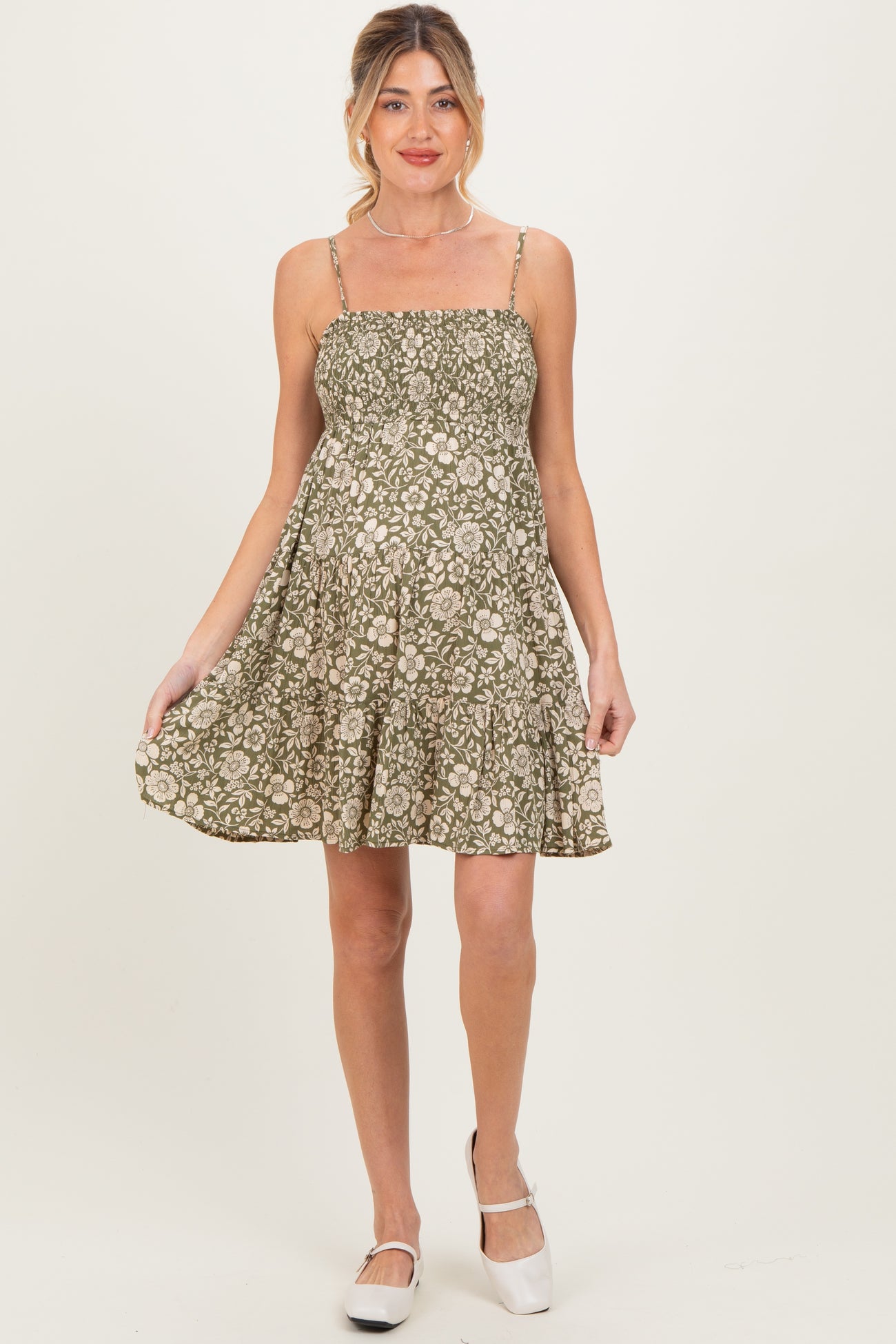 woman wearing a green floral maternity dress with adjustable straps and a flared skirt, showcasing her baby bump