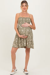 woman wearing a green floral maternity dress with adjustable straps and holding her baby bump