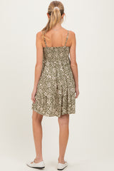 woman wearing a green floral maternity dress with adjustable straps and a relaxed fit, standing with her back to the camera