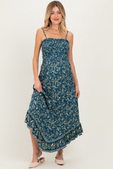 woman wearing a teal floral maternity maxi dress with adjustable straps and ruffle hem, showcasing her baby bump