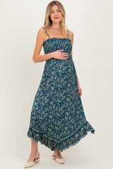 woman wearing a teal floral maternity maxi dress with adjustable straps and a ruffled hem, holding her baby bump