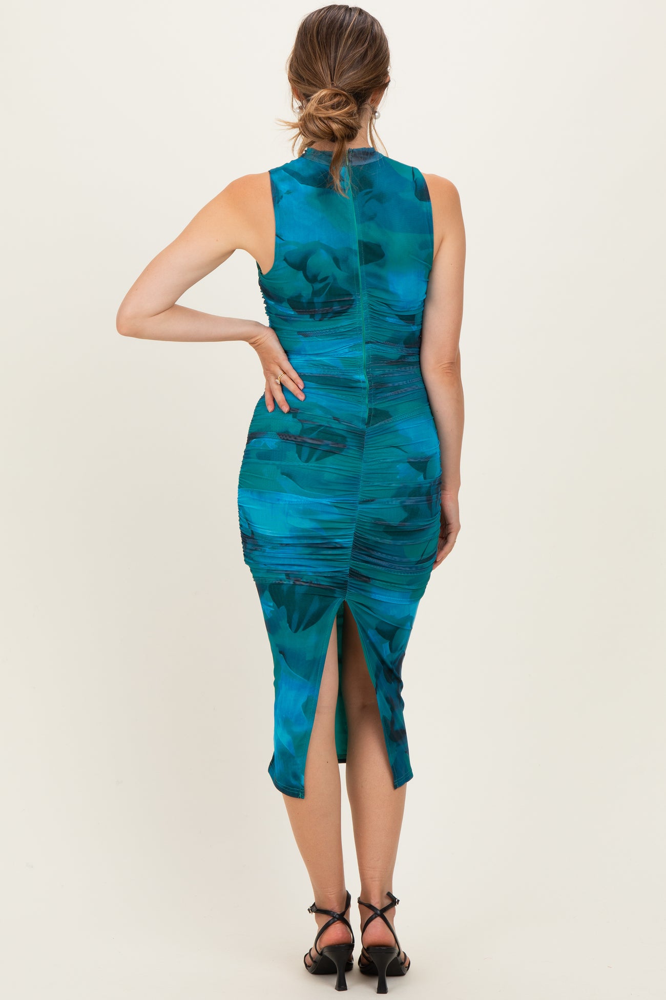 woman wearing a teal maternity dress with ruching and a slit at the back, styled with strappy black heels