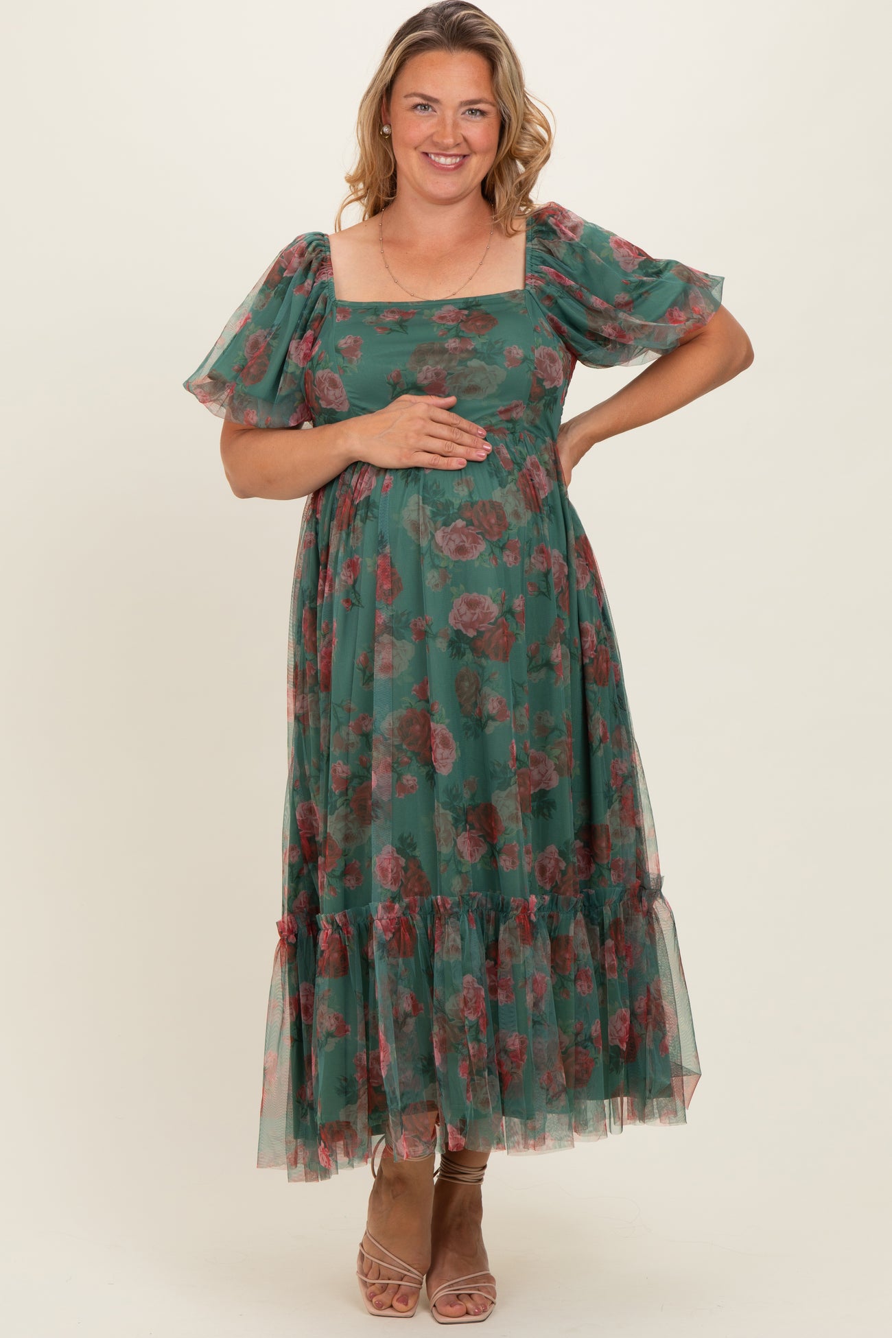woman wearing a green floral maternity maxi dress with puff sleeves and holding her baby bump